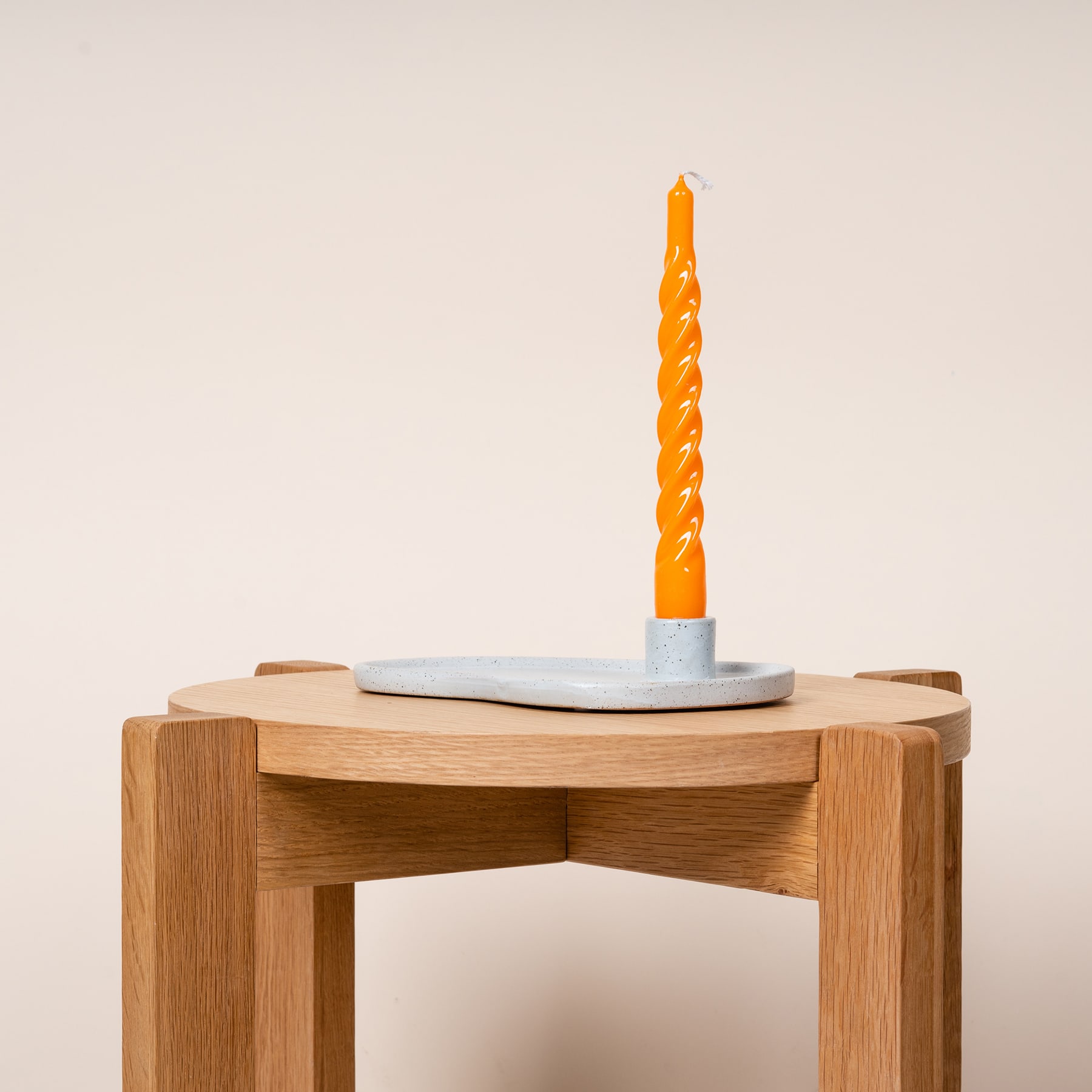 Eine einzelne orangefarbene Spiralkerze steht auf einer Holzplattform vor einem schlichten, hellen Hintergrund.