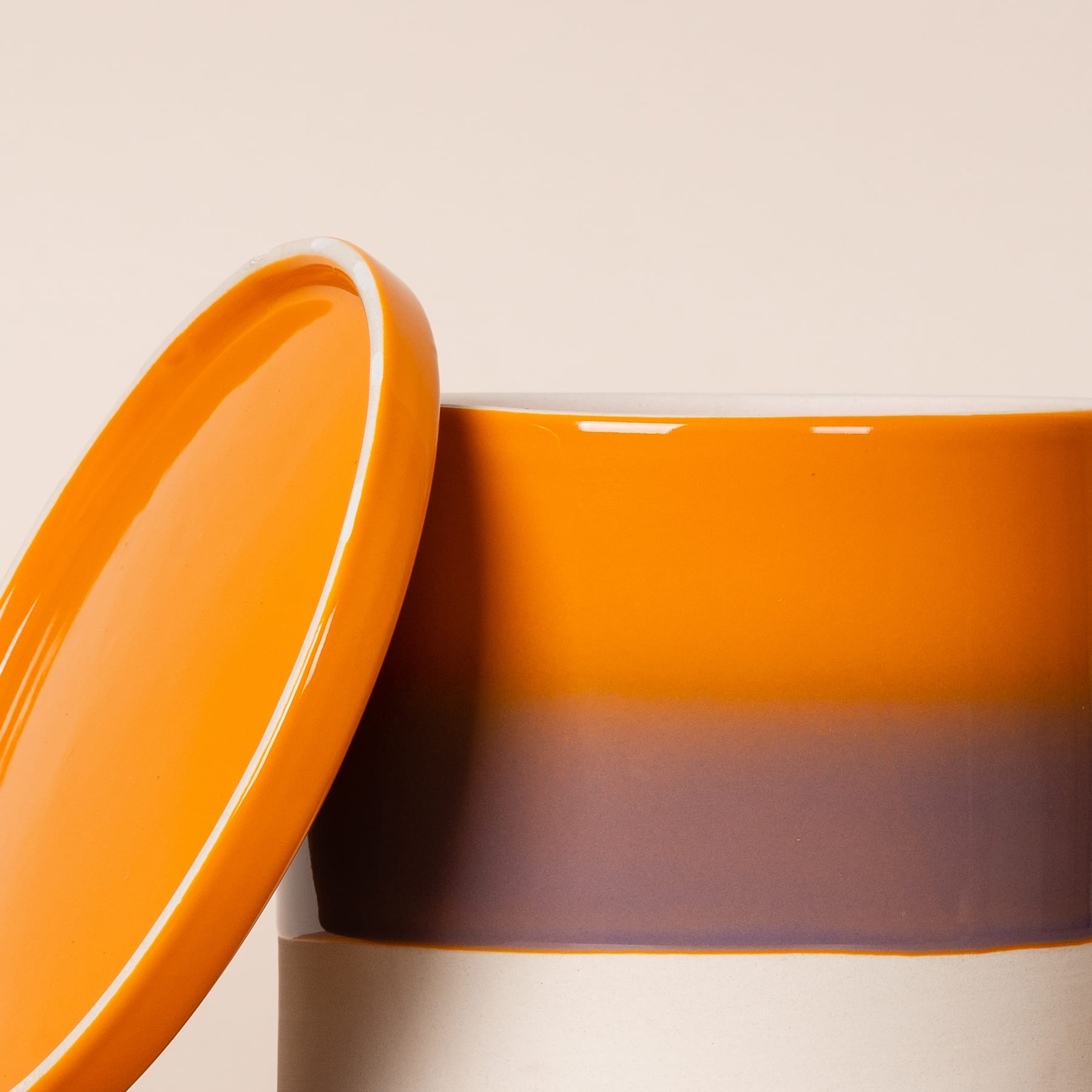 Eine leuchtend orangefarbene Keramikschüssel mit Deckel steht auf einer Oberfläche in neutraler Farbe und wirft einen weichen Schatten.
