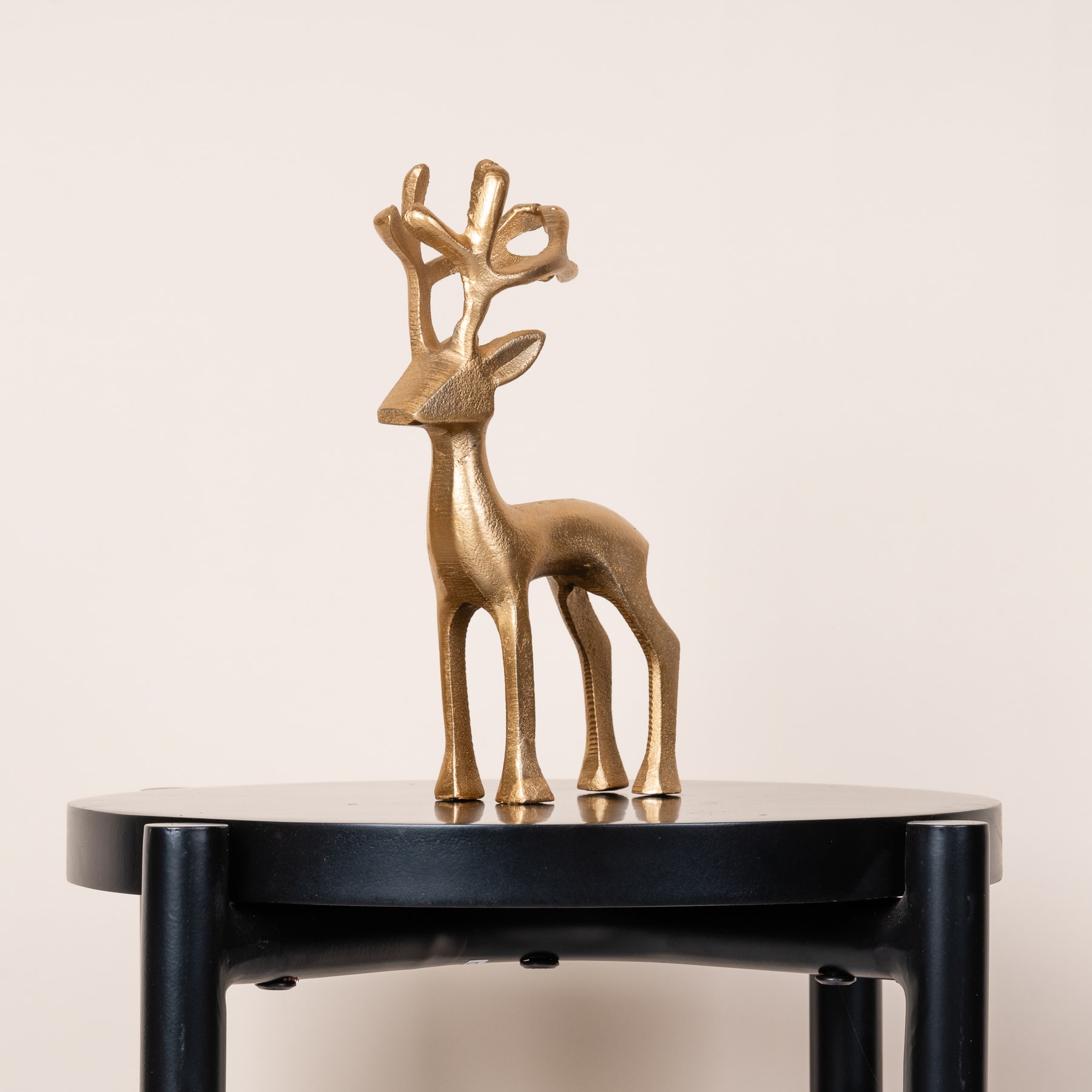 Eine goldene, abstrakte, hirschähnliche Skulptur steht auf einem schwarzen Sockel vor einem schlichten, hellen Hintergrund.