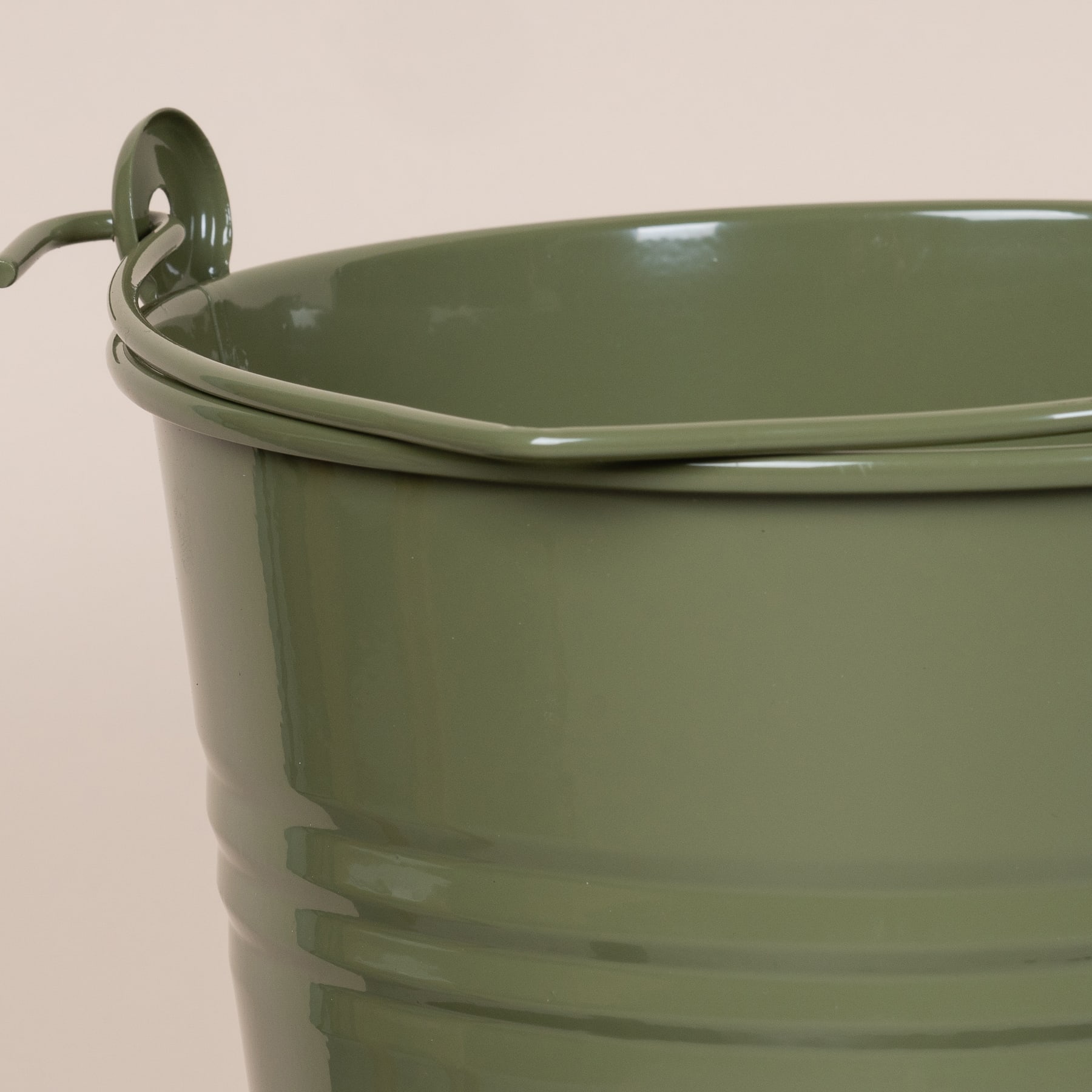 Ein grüner Metalleimer oder -behälter mit Griff vor einem schlichten beigen Hintergrund.