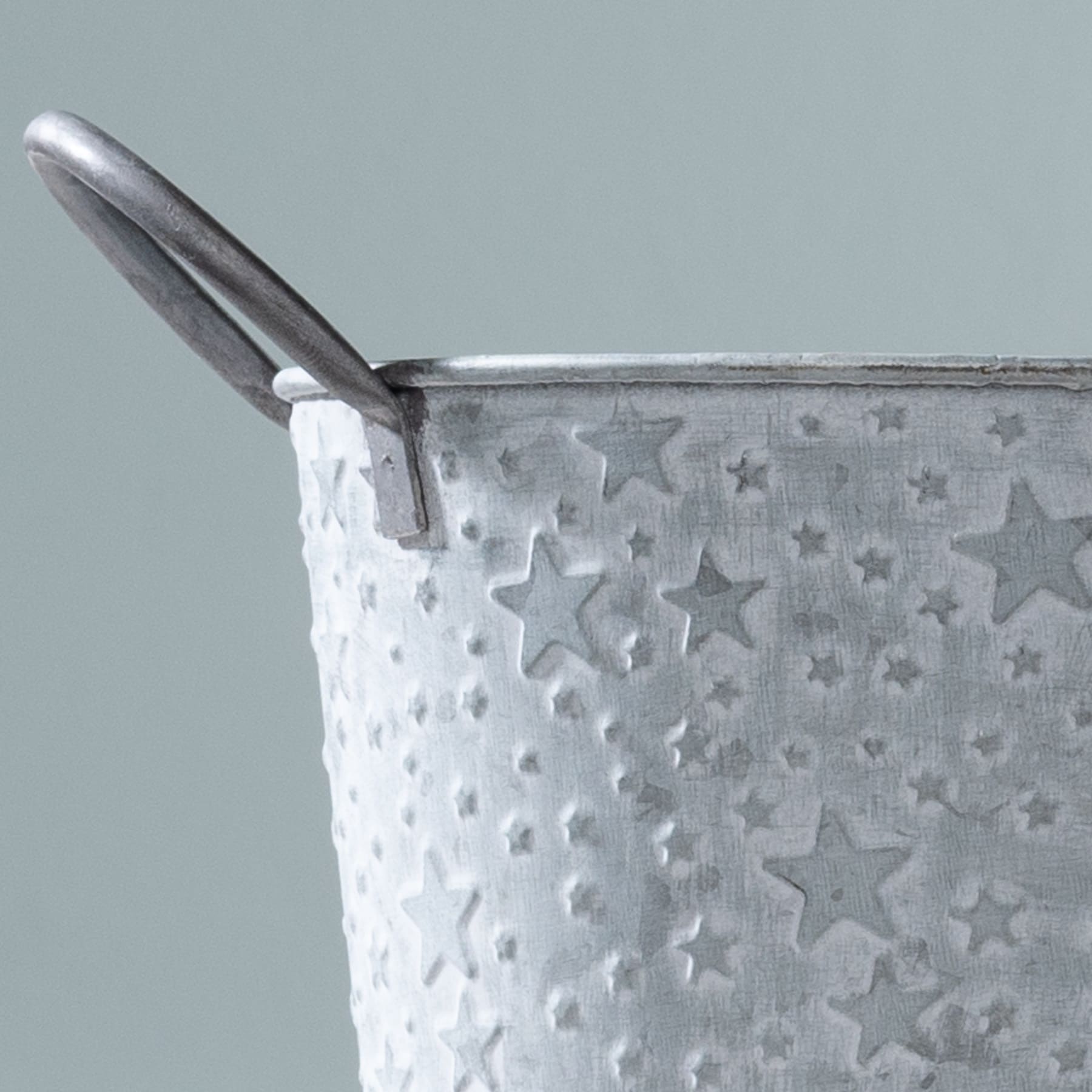 Vor einem schlichten grauen Hintergrund steht ein Metallbehälter mit sternenförmiger Oberfläche.