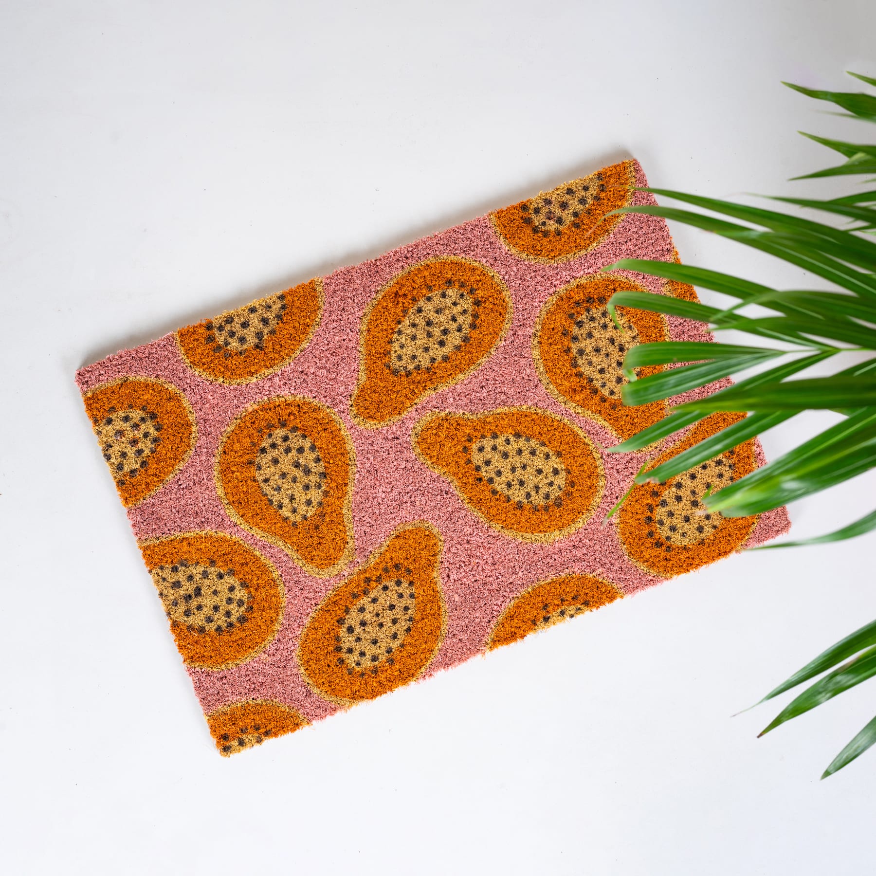Das Bild zeigt ein lebendiges, tropisch inspiriertes Muster mit großen, orangefarbenen Papaya- oder Drachenfruchtformen vor einem rosa Hintergrund, wobei üppige grüne Blätter die Komposition einrahmen.