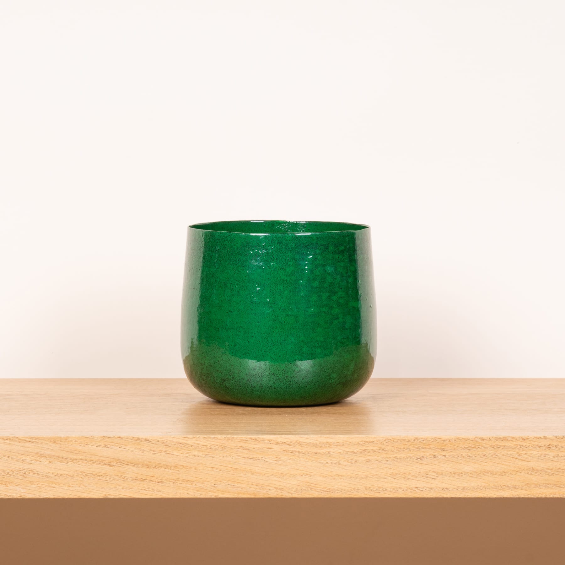 Eine grüne Keramiktasse oder -schüssel steht auf einer Holzoberfläche vor einem schlichten Hintergrund.