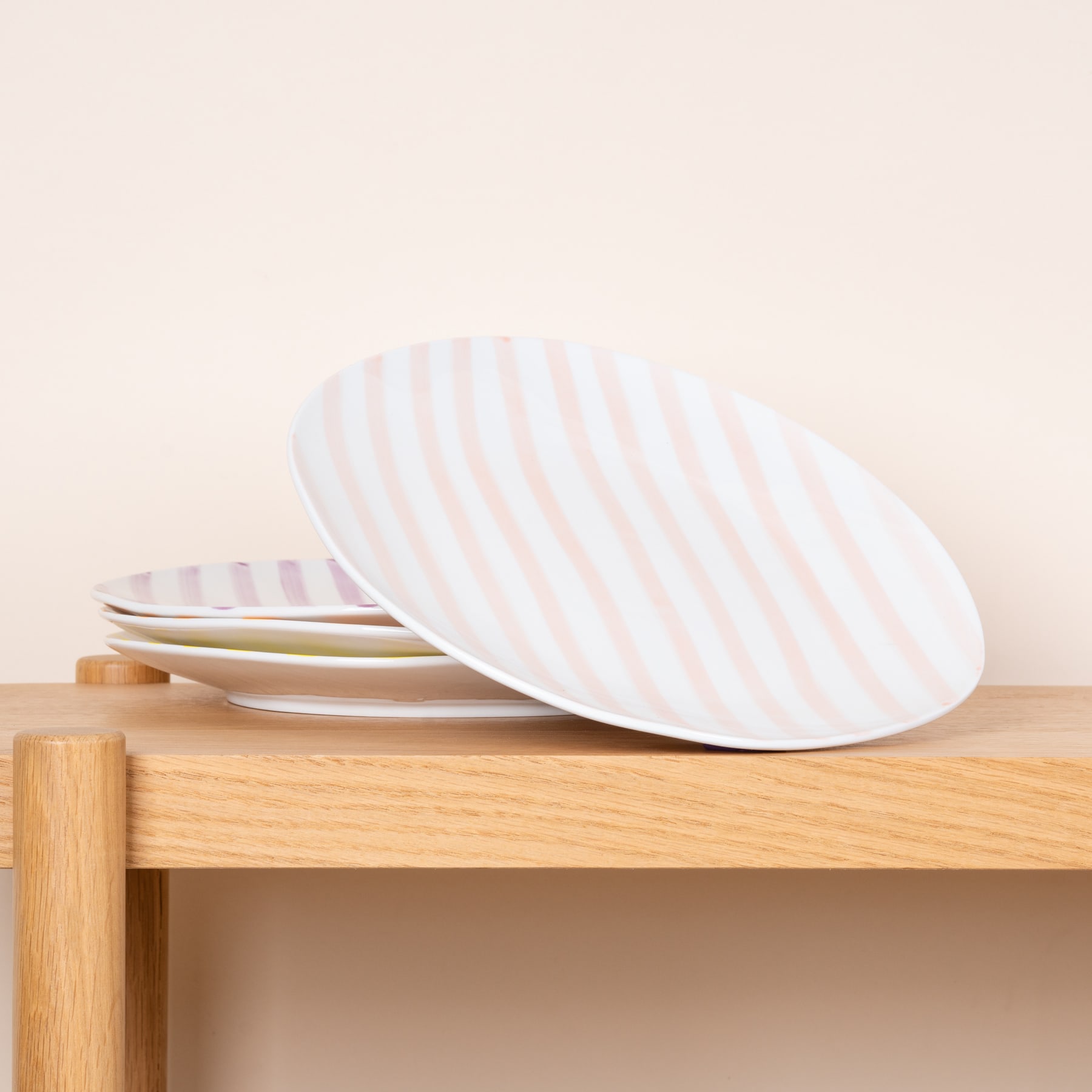 Ein Stapel weißer ovaler Teller liegt auf einer Holzoberfläche mit schlichtem Hintergrund.