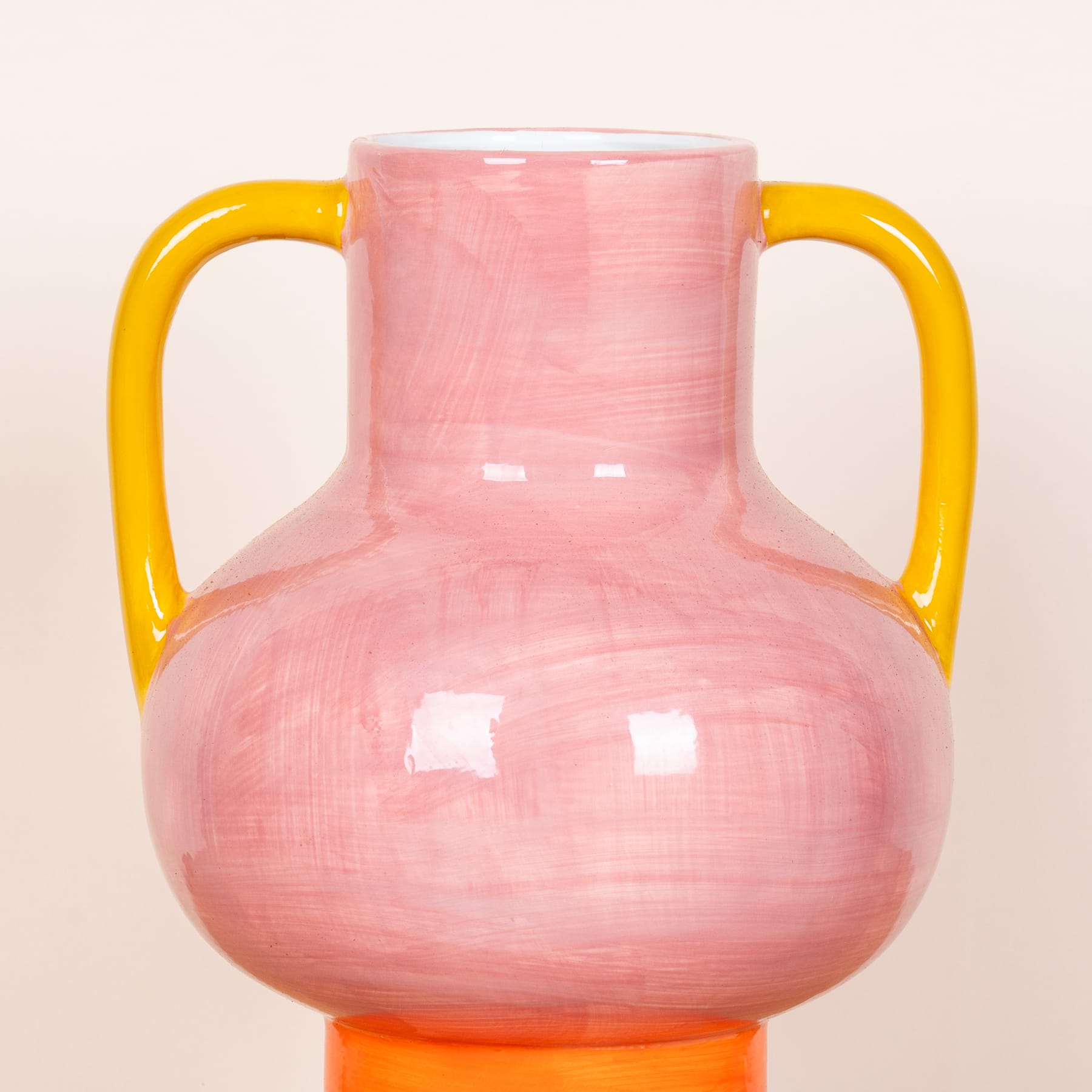 Eine rosa Keramikvase mit gelben Griffen steht vor einem schlichten weißen Hintergrund.