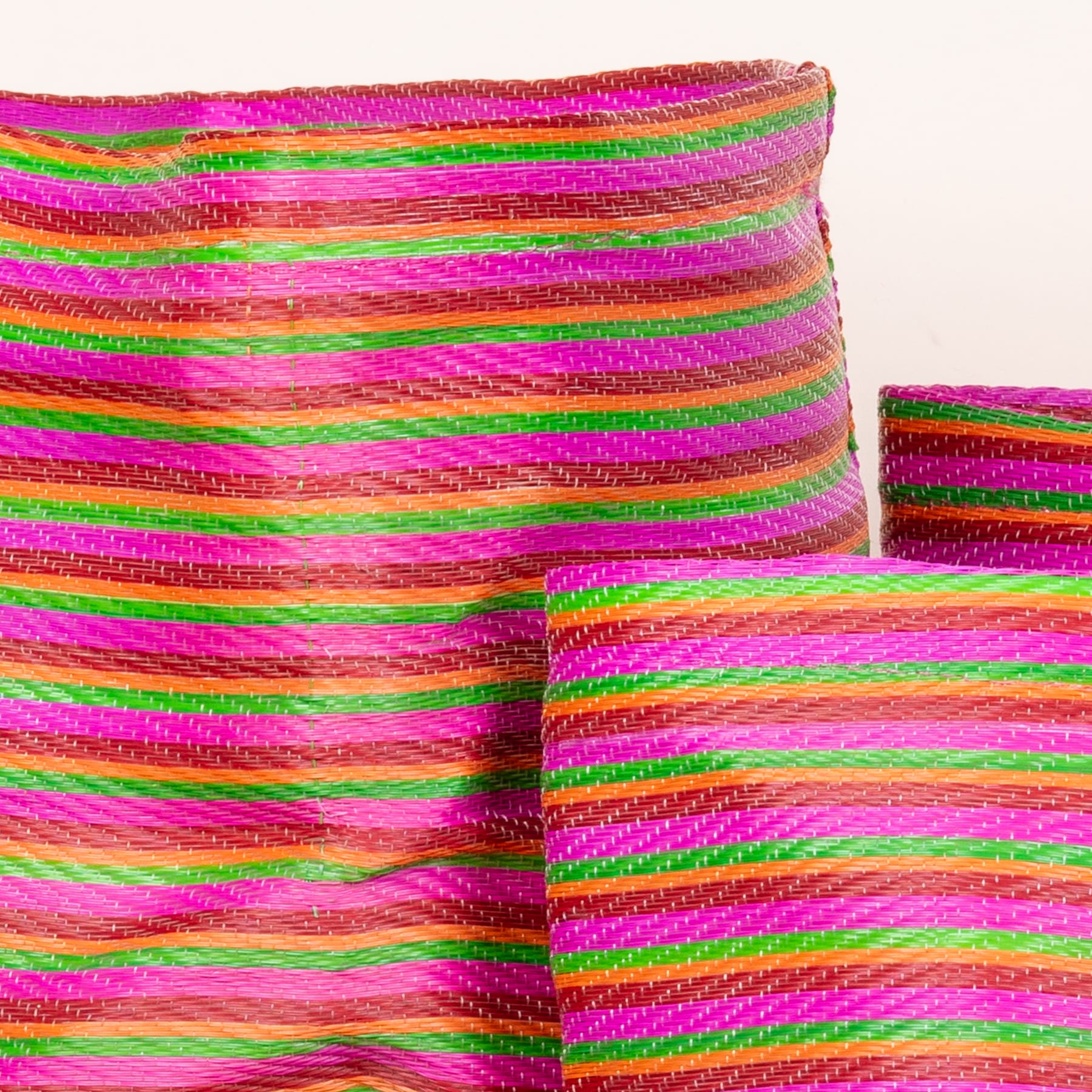 Lebendiger, mehrfarbiger Webstoff mit kräftigen, sich kreuzenden diagonalen Streifen in Rosa-, Grün- und Orangetönen.