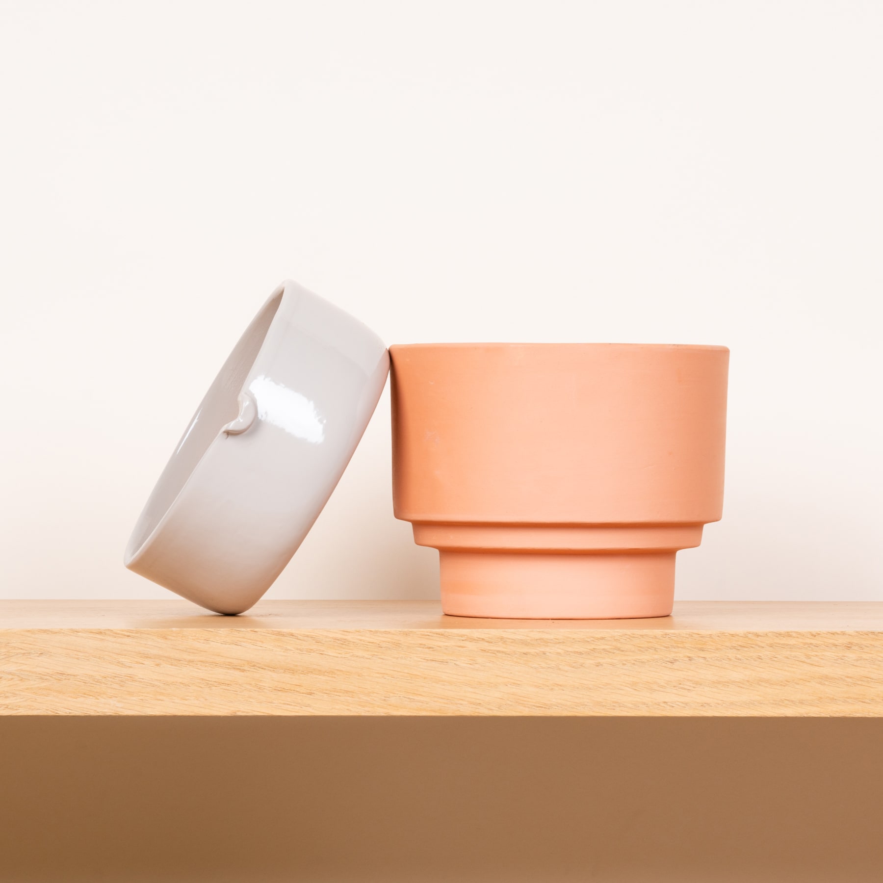Zwei Keramikschalen, eine weiße und eine pfirsichfarbene, stehen auf einer Holzoberfläche vor einem schlichten Hintergrund.