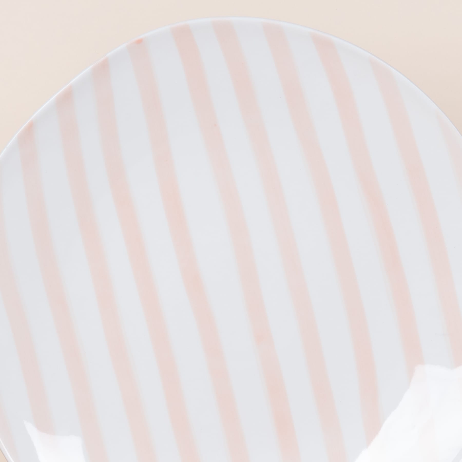 Eine runde Platte oder Oberfläche mit zarten, pastellfarbenen vertikalen Streifen in Rosa- und Weißtönen, die einen weichen, ruhigen visuellen Effekt erzeugen.