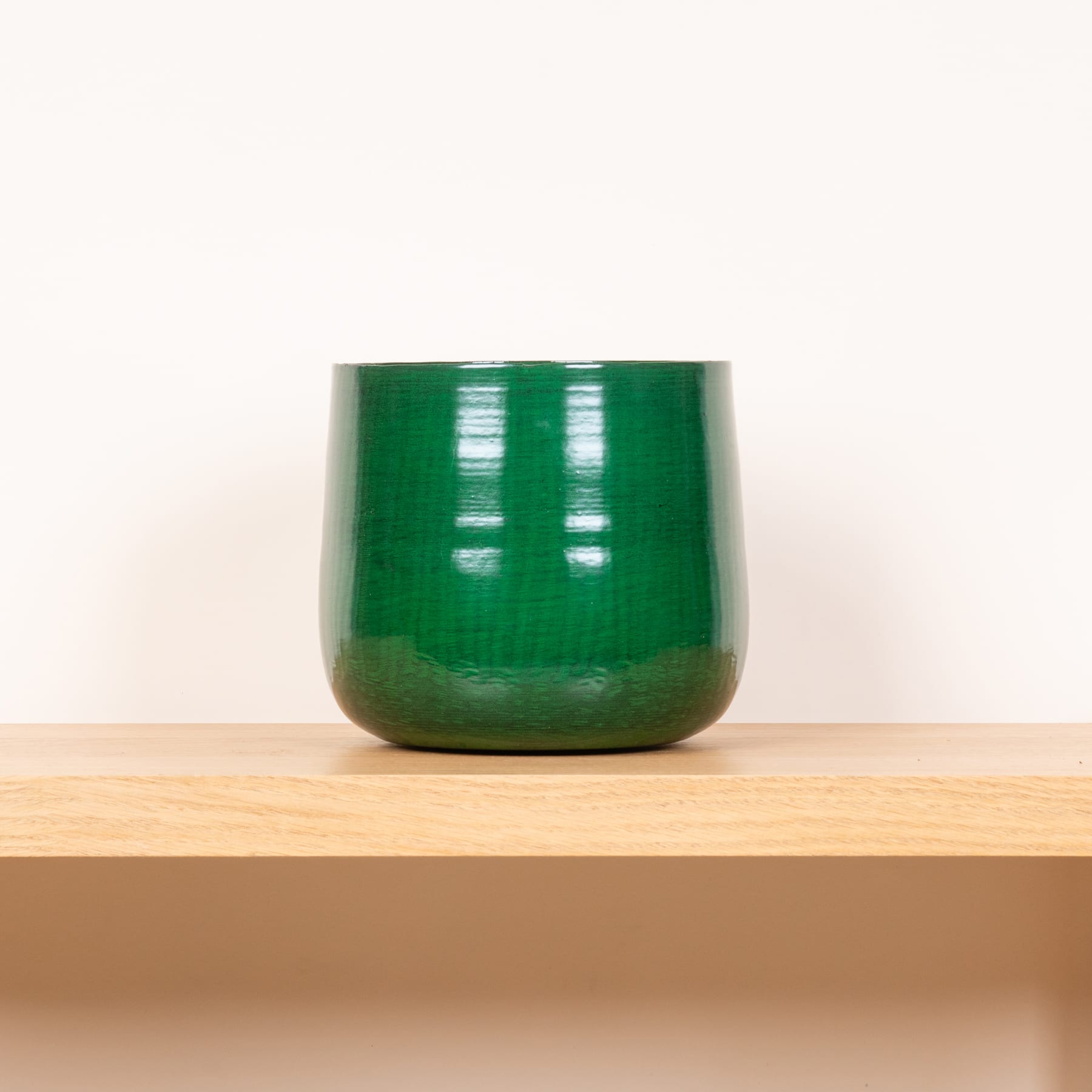 Eine grüne Glasschale steht auf einem Holzregal vor einem schlichten weißen Hintergrund.