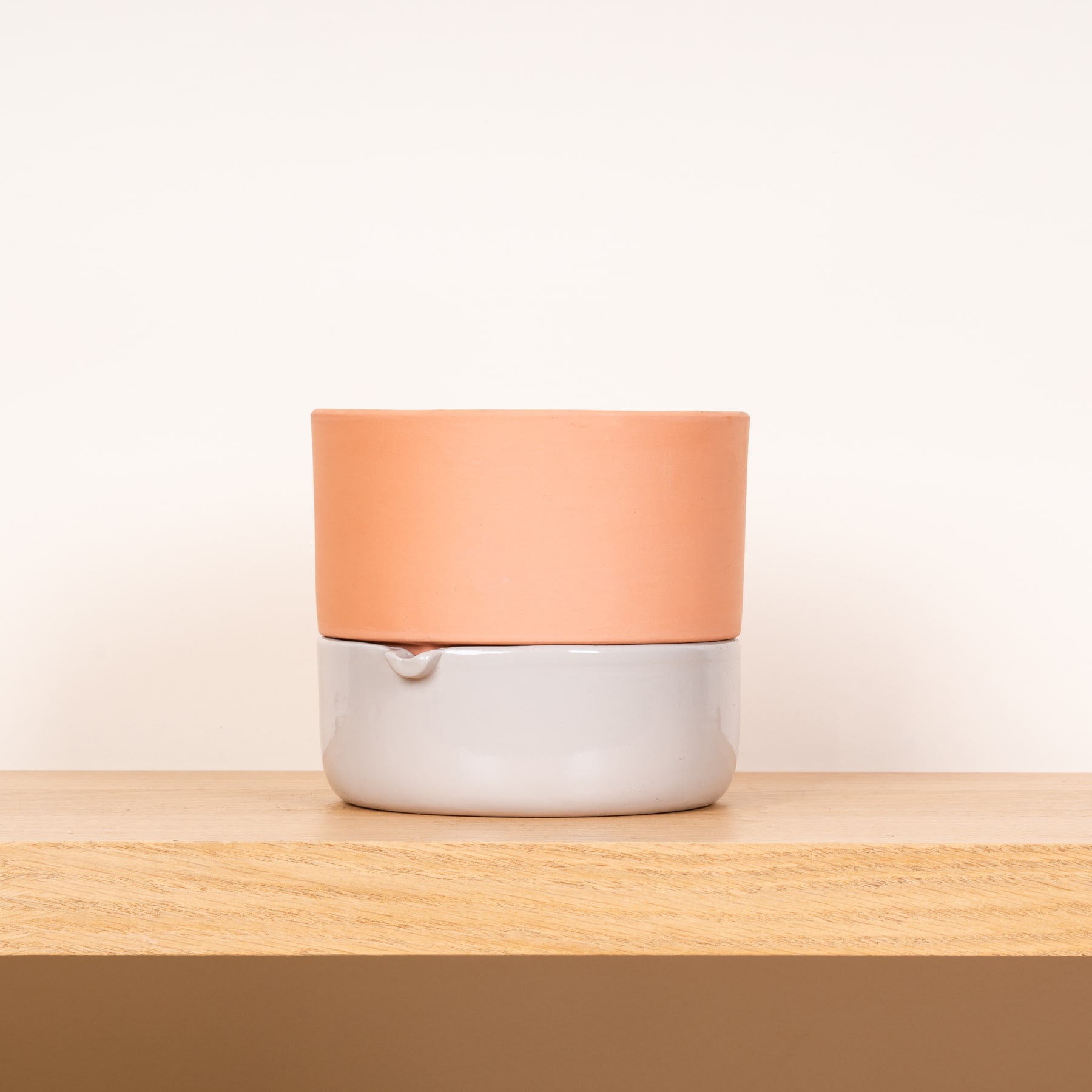 Ein pfirsichfarbener zylindrischer Behälter steht auf einer Holzoberfläche vor einem schlichten weißen Hintergrund.
