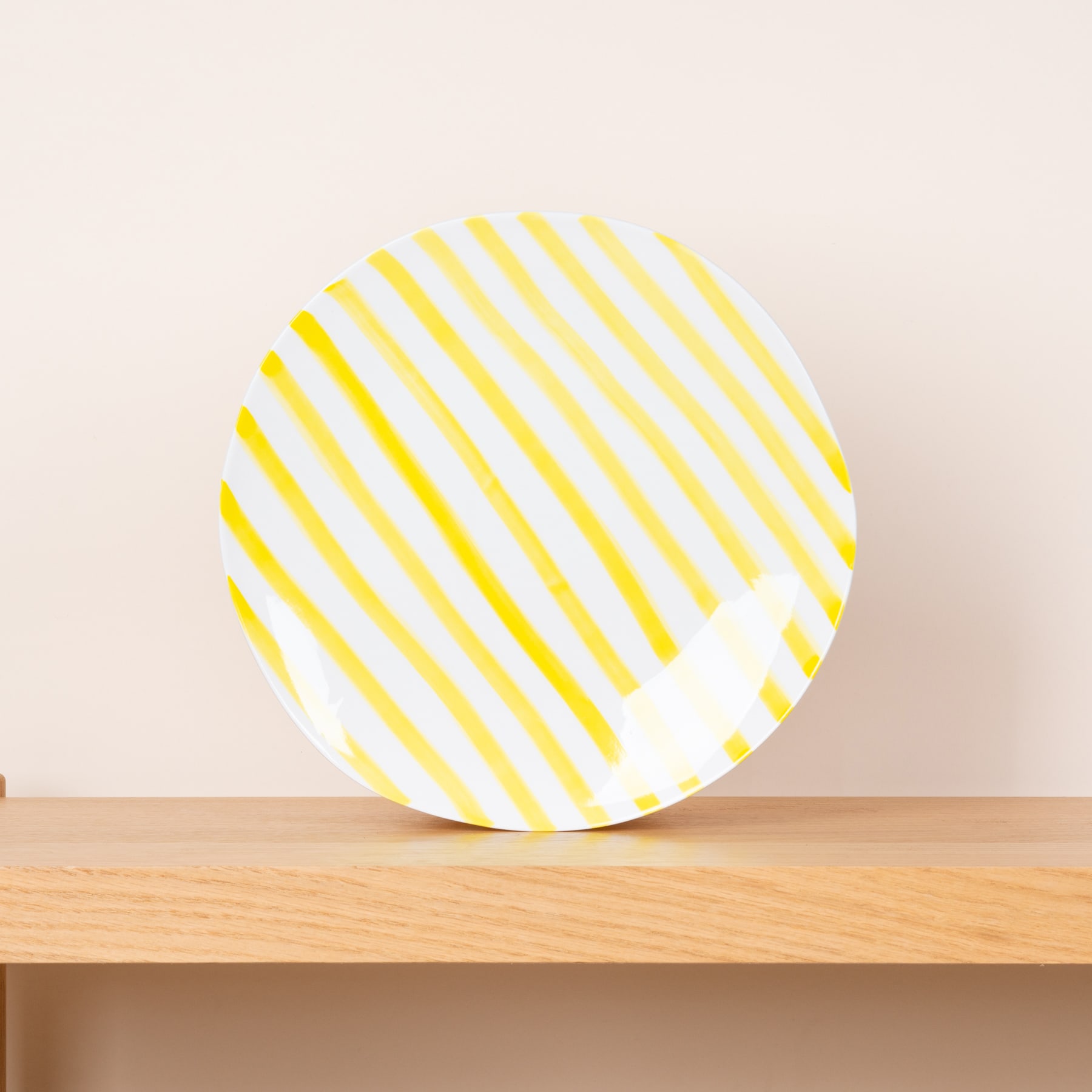 Ein runder, gelb-weiß gestreifter Teller oder eine Platte steht auf einem Holztisch vor einer schlichten, hellen Wand.