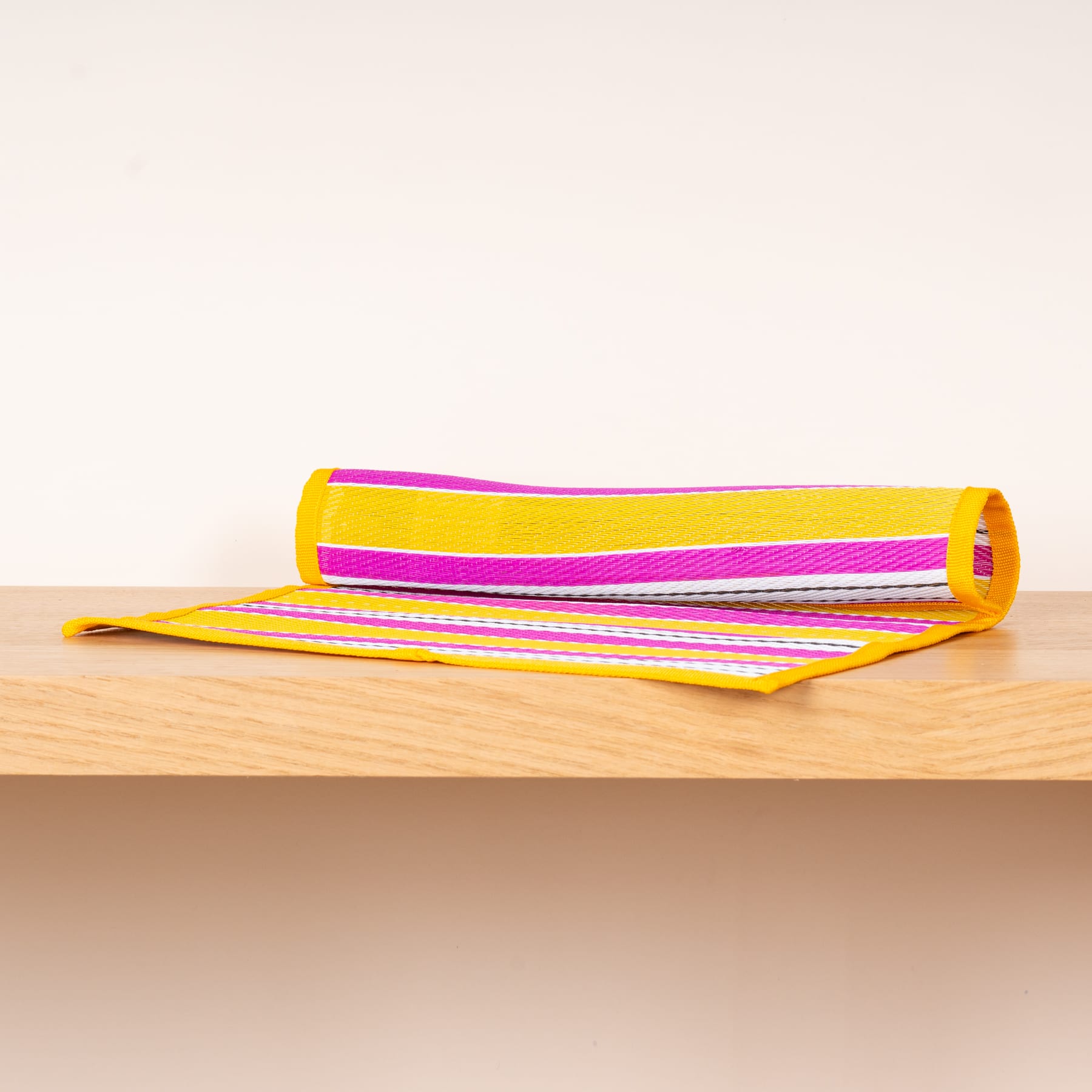 Ein Stapel bunt gestreifter Handtücher oder Decken liegt auf einer Holzoberfläche vor einem schlichten Hintergrund.