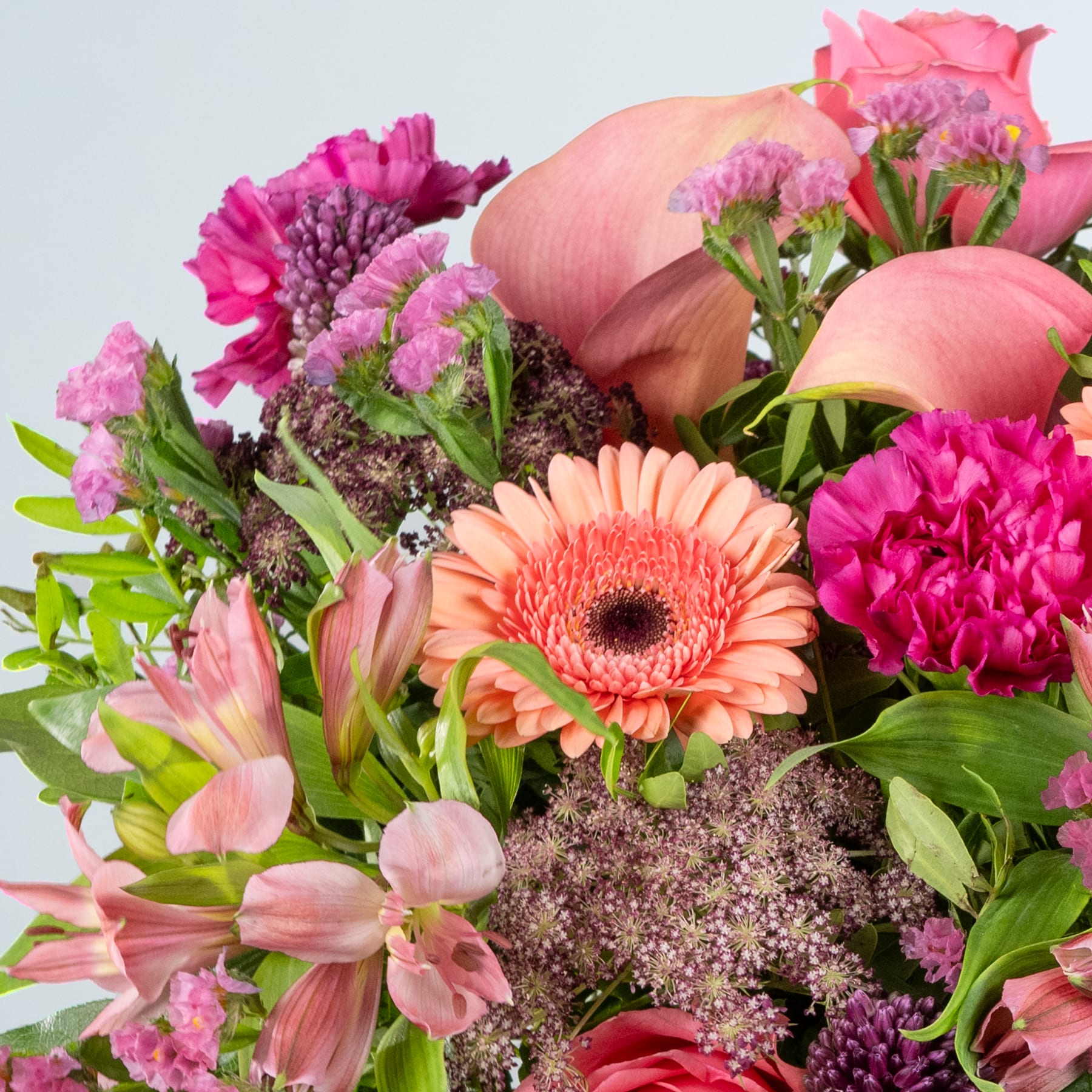 Ein lebendiger Strauß verschiedener rosa und orangefarbener Blumen, darunter Rosen, Nelken und Gerbera, arrangiert vor einem schlichten hellen Hintergrund.