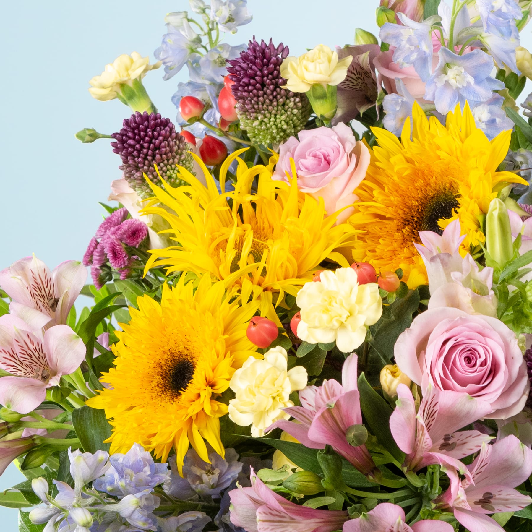 Ein lebendiger Strauß aus gelben Sonnenblumen, rosa Rosen und verschiedenen anderen bunten Blumen vor einem sanften blauen Hintergrund.