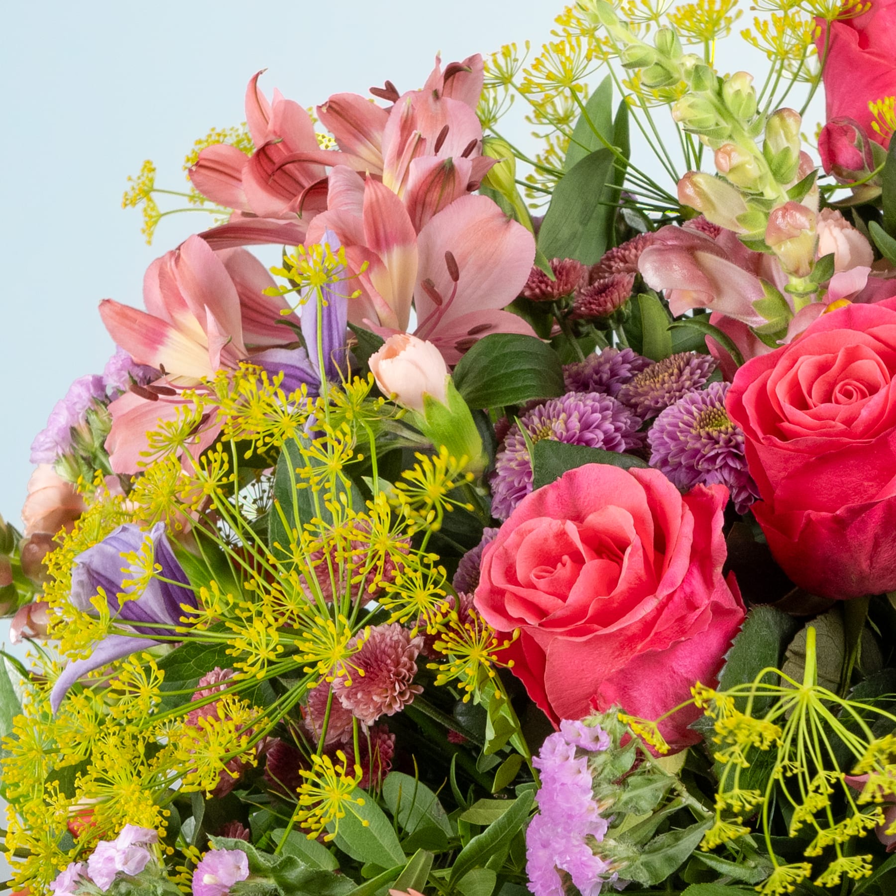Ein lebendiger Strauß verschiedener bunter Blumen, darunter rosa Lilien, rote Rosen und gelbe Gänseblümchen, vor einem hellblauen Hintergrund.