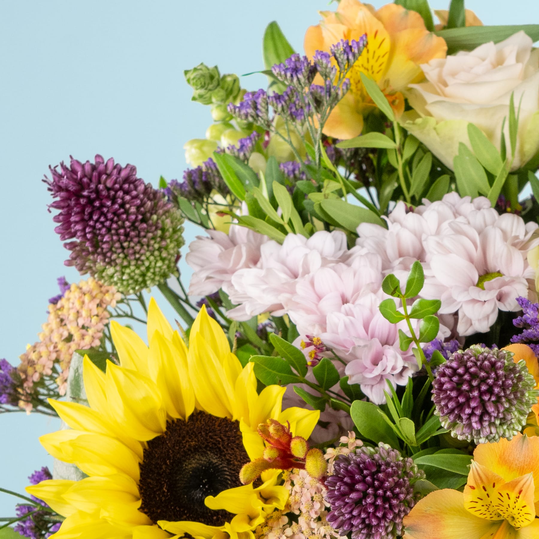 Ein lebendiger Strauß bunter Blumen, darunter Sonnenblumen, Chrysanthemen und Rosen, vor einem sanften blauen Hintergrund.