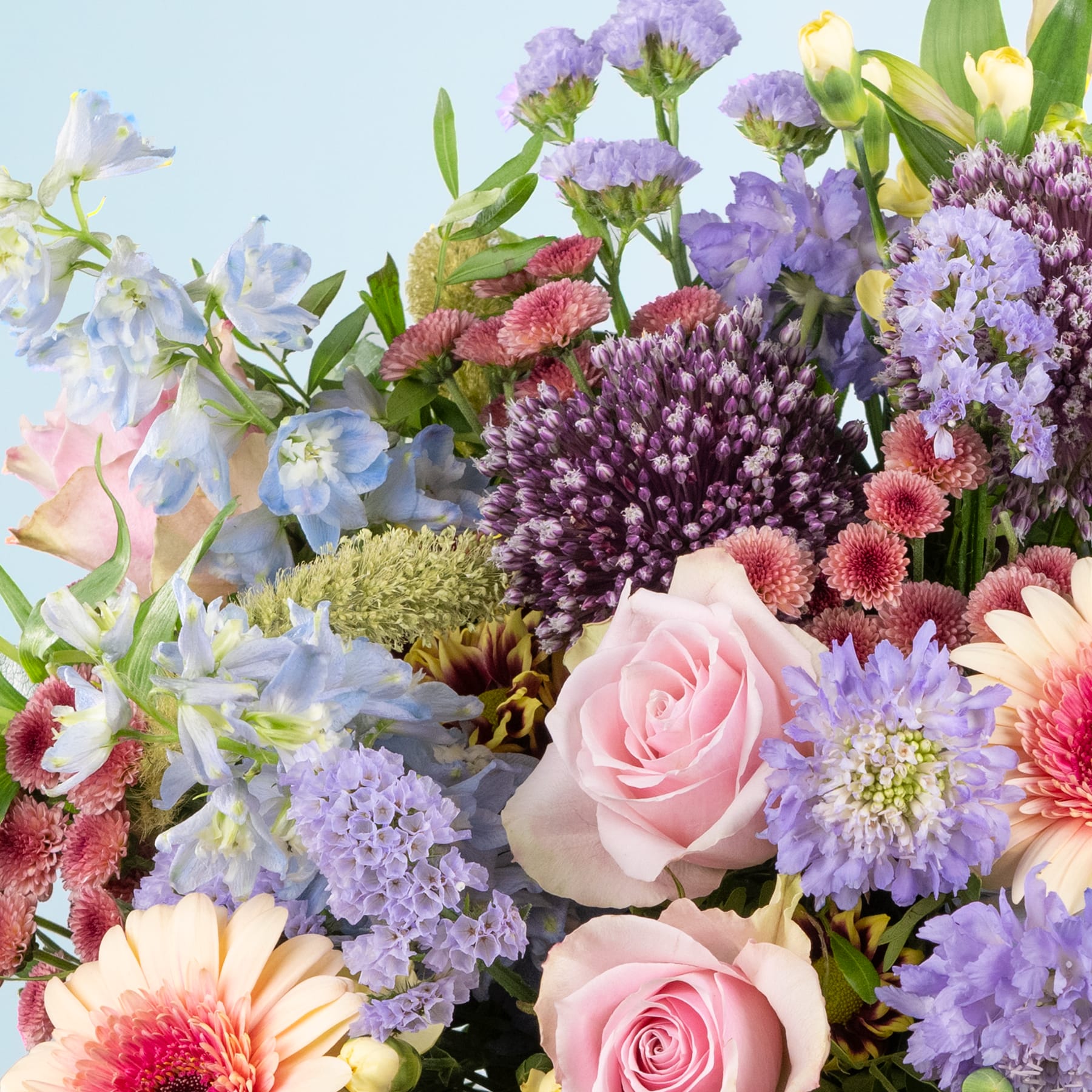 Ein lebendiger Strauß verschiedener bunter Blumen, darunter rosa Rosen, lila Chrysanthemen und gelbe Narzissen, vor einem sanften blauen Hintergrund.
