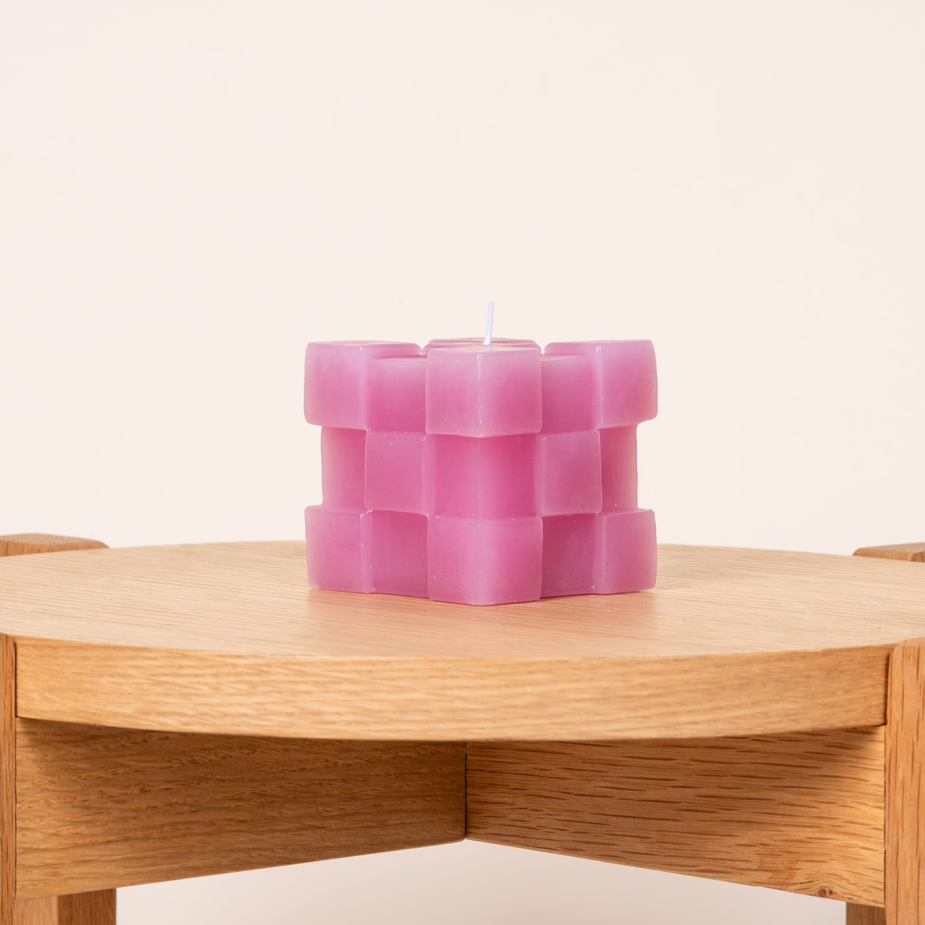 Eine rosafarbene Kerze mit geometrischem Muster steht auf einem Holztisch vor einem schlichten, hellen Hintergrund.