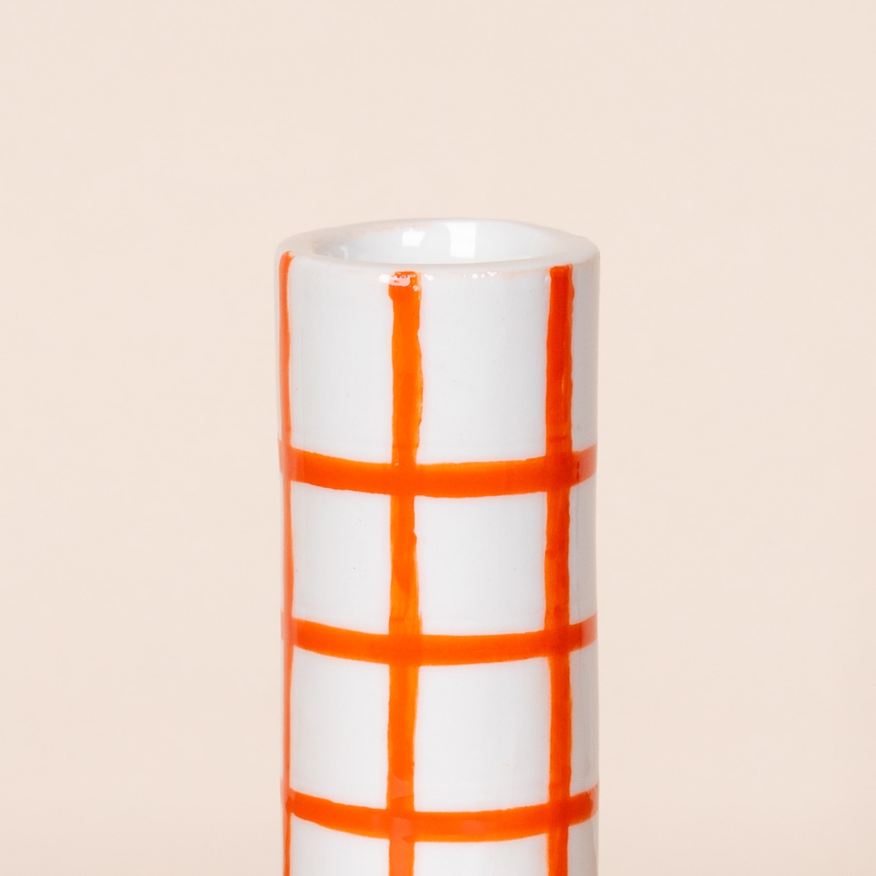 Eine weiße Keramiktasse mit einem orangefarbenen Gittermuster auf der Oberfläche vor einem hellbeigen Hintergrund.