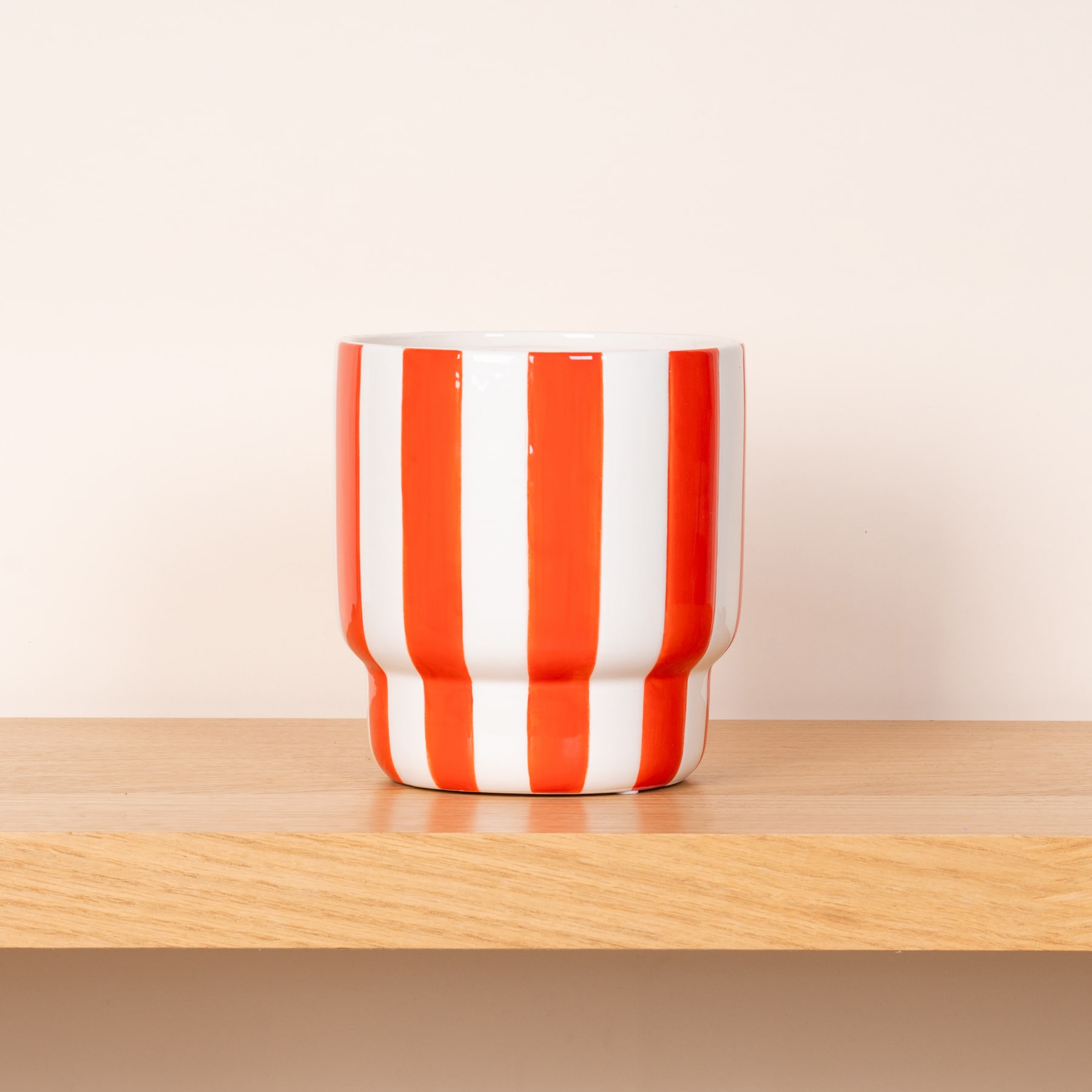 Eine farbenfrohe, gestreifte Keramiktasse oder -becher steht auf einer Holzoberfläche vor einem schlichten, hellen Hintergrund.