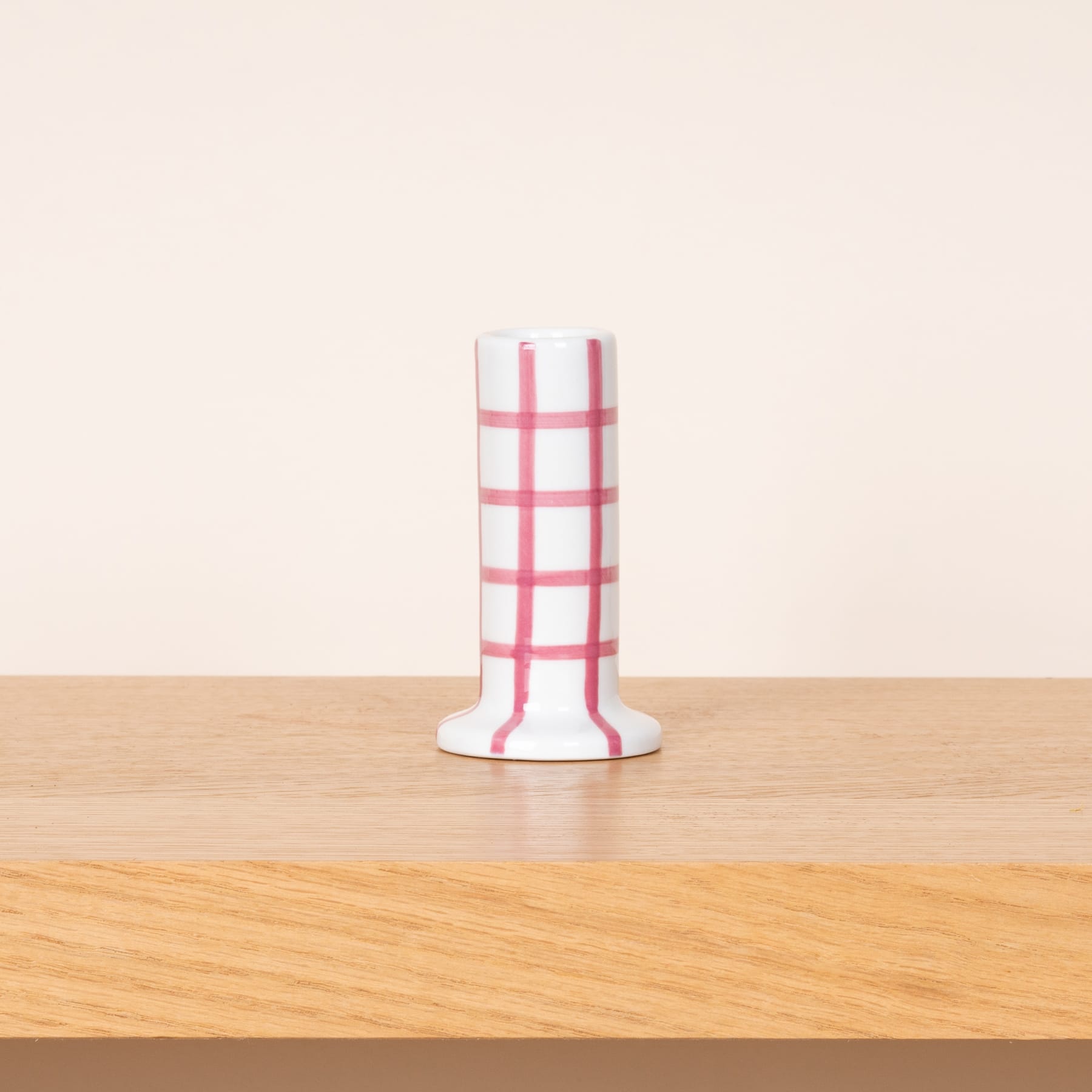 Eine weiß-rot gestreifte Vase oder ein Behälter steht auf einem Holztisch vor einem schlichten, hellen Hintergrund.