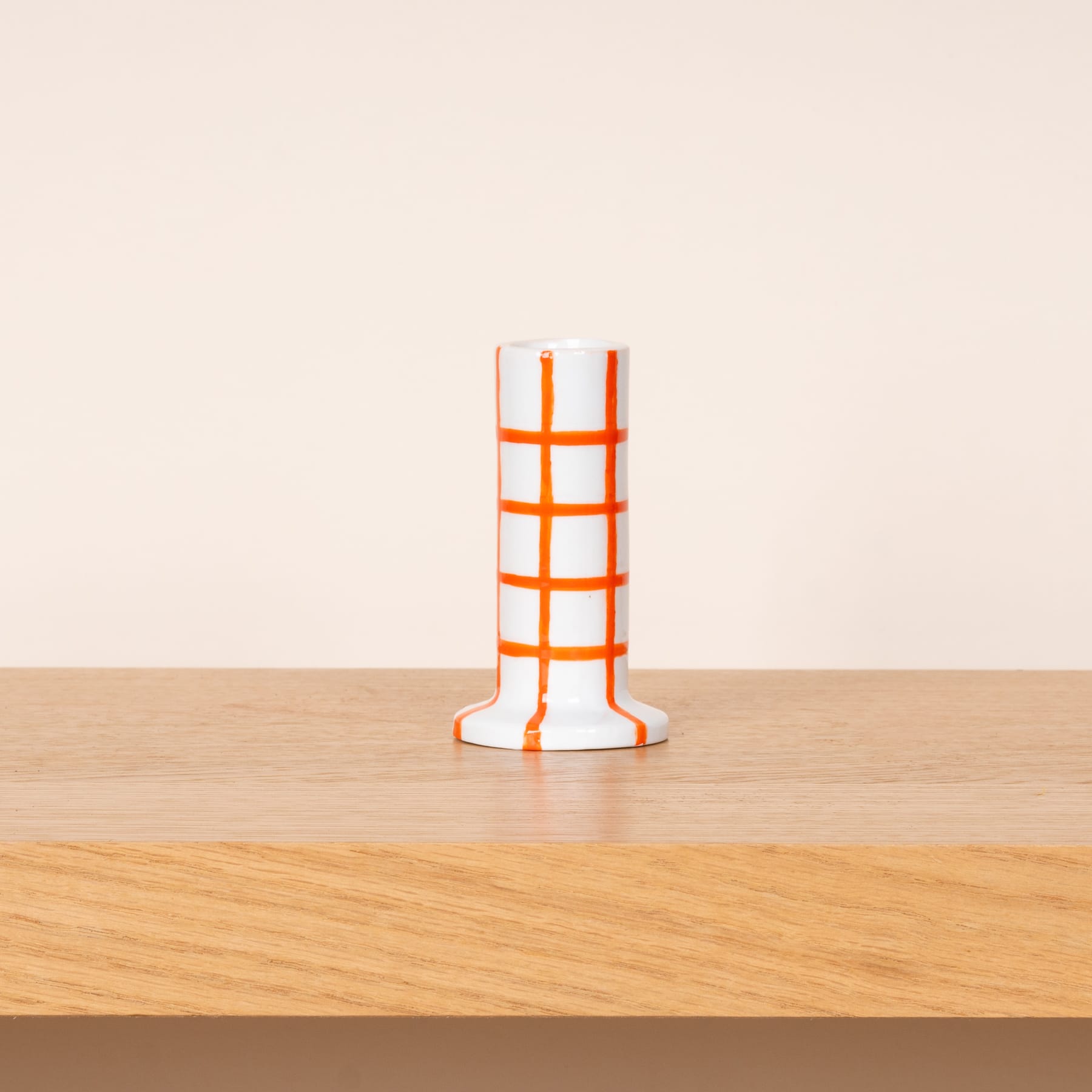 Eine weiß-orangefarbene geometrische Vase oder Skulptur steht auf einem Holztisch vor einem schlichten Hintergrund.
