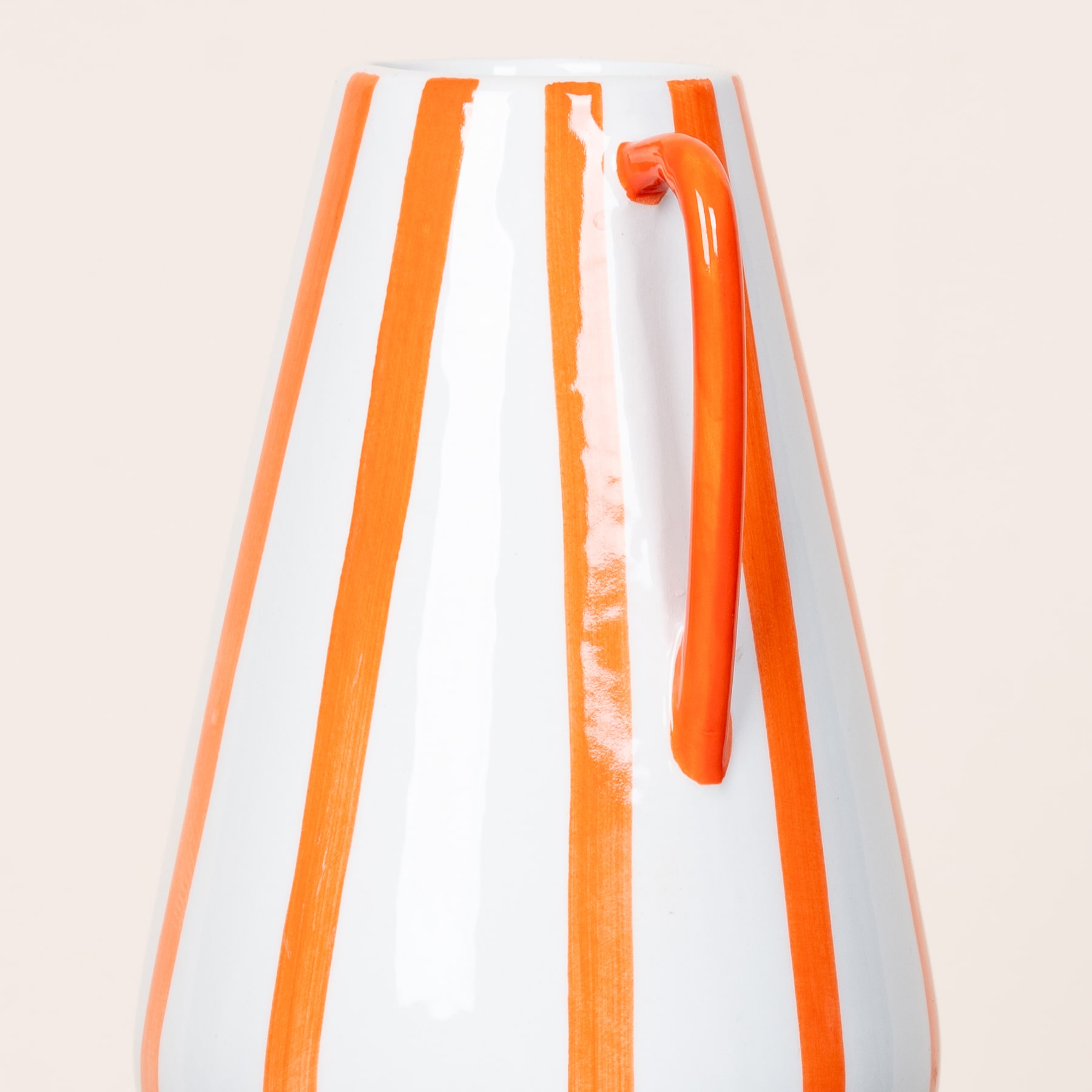 Eine weiß-orange gestreifte Vase oder ein Behälter mit orangefarbenem Griff steht vor einem schlichten, hellen Hintergrund.