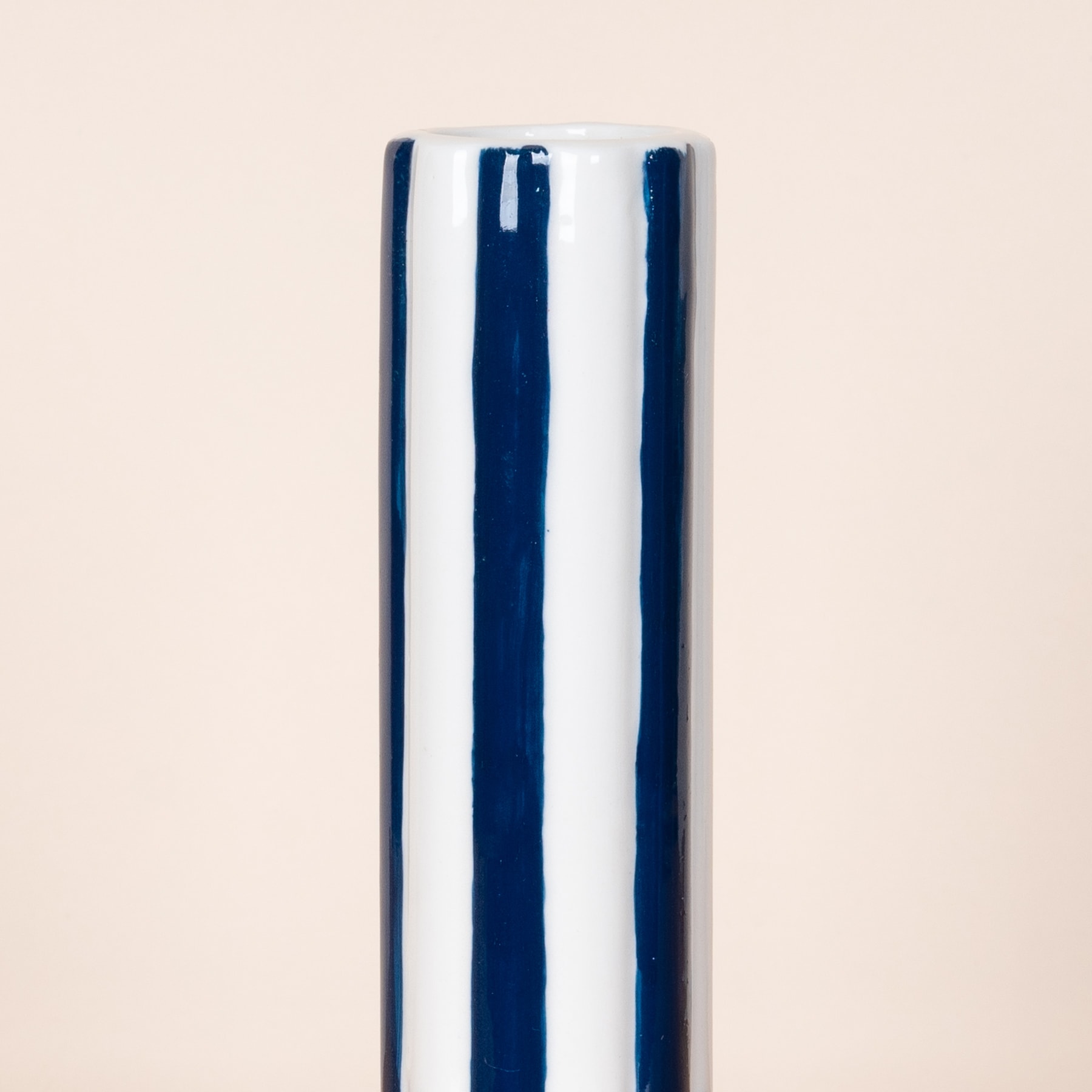 Eine zylindrische Keramikvase mit abwechselnd marineblauen und weißen vertikalen Streifen auf einem schlichten beigen Hintergrund.