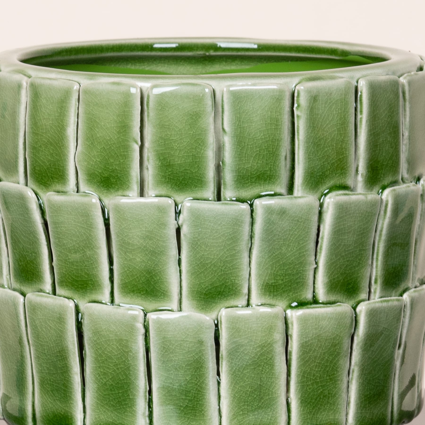 Ein grüner Blumentopf oder eine Vase aus Keramik mit einem strukturierten Kachelmuster auf der Oberfläche vor einem schlichten Hintergrund.