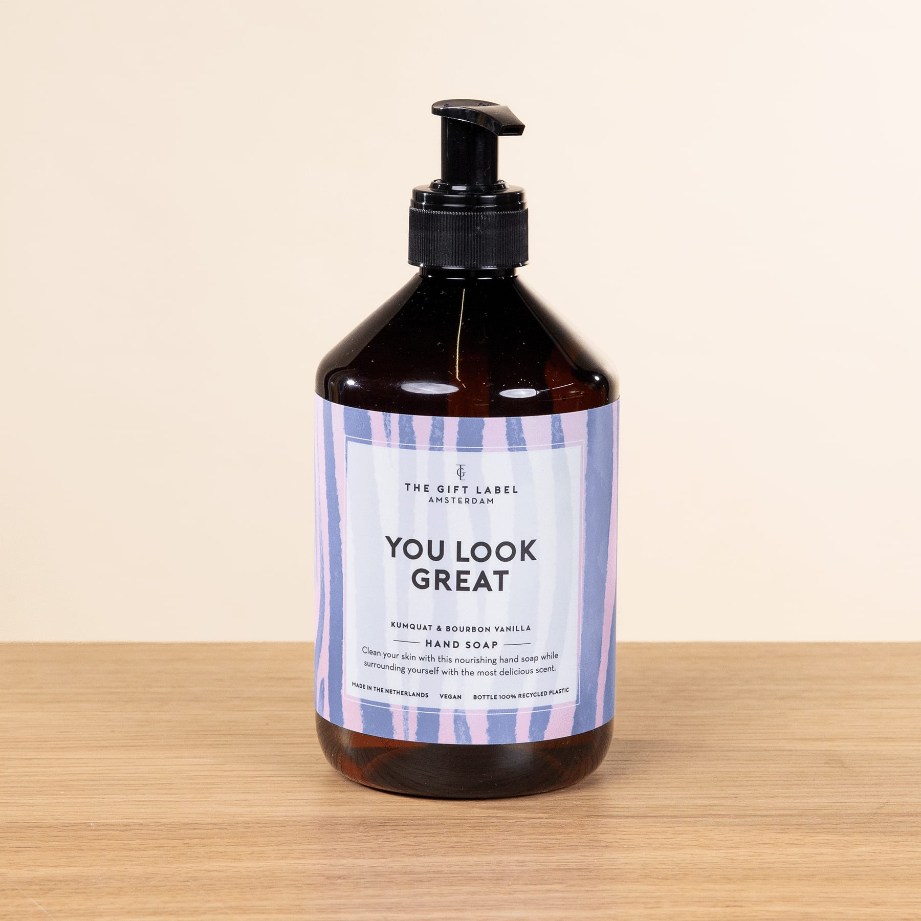 Eine schwarze Flasche mit Pumpspender und der Aufschrift „Du siehst toll aus“ steht auf einer Holzoberfläche vor einem hellen Hintergrund.