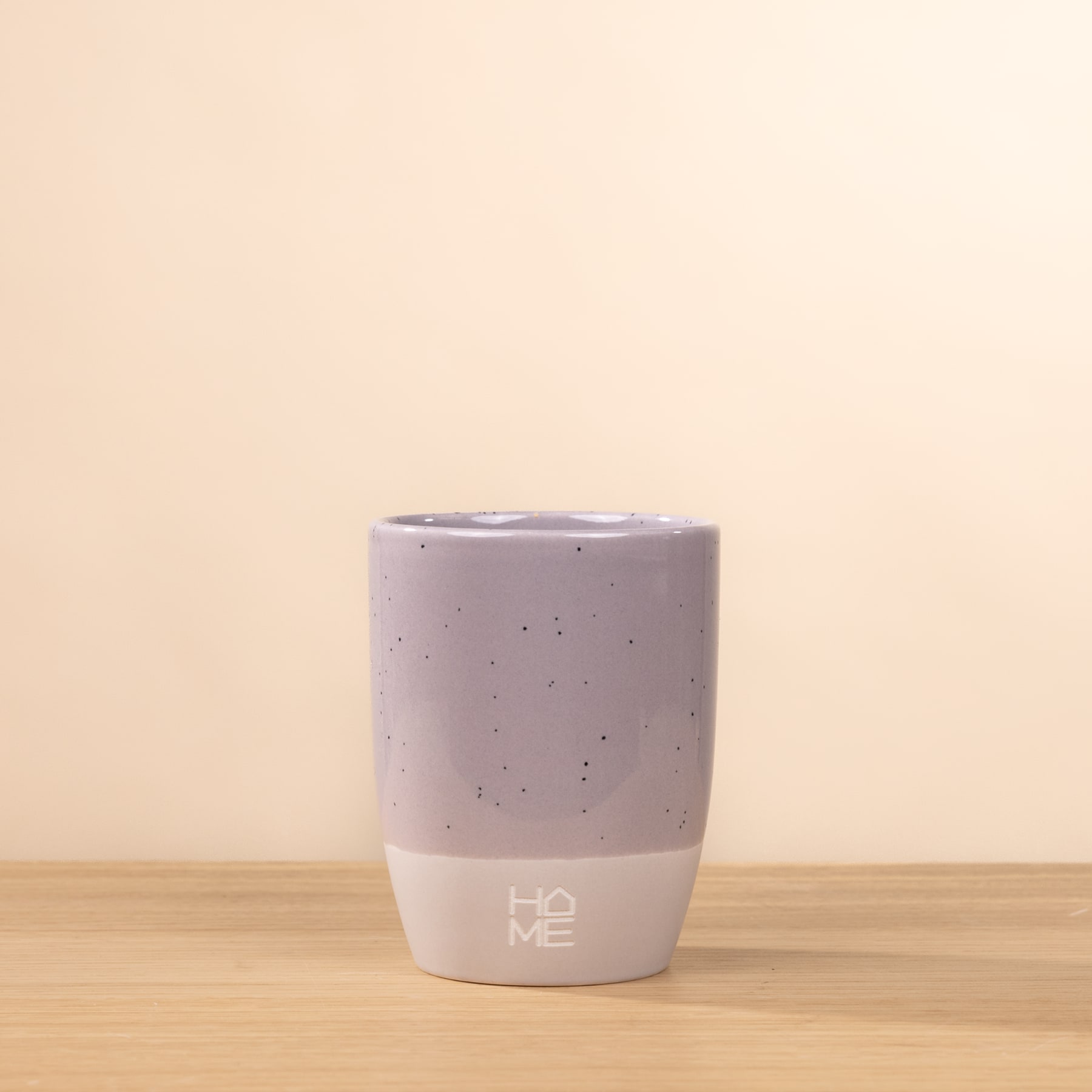 Ein einfacher, heller Keramikbecher oder eine Tasse steht auf einer Holzoberfläche vor einem schlichten, beigen Hintergrund.