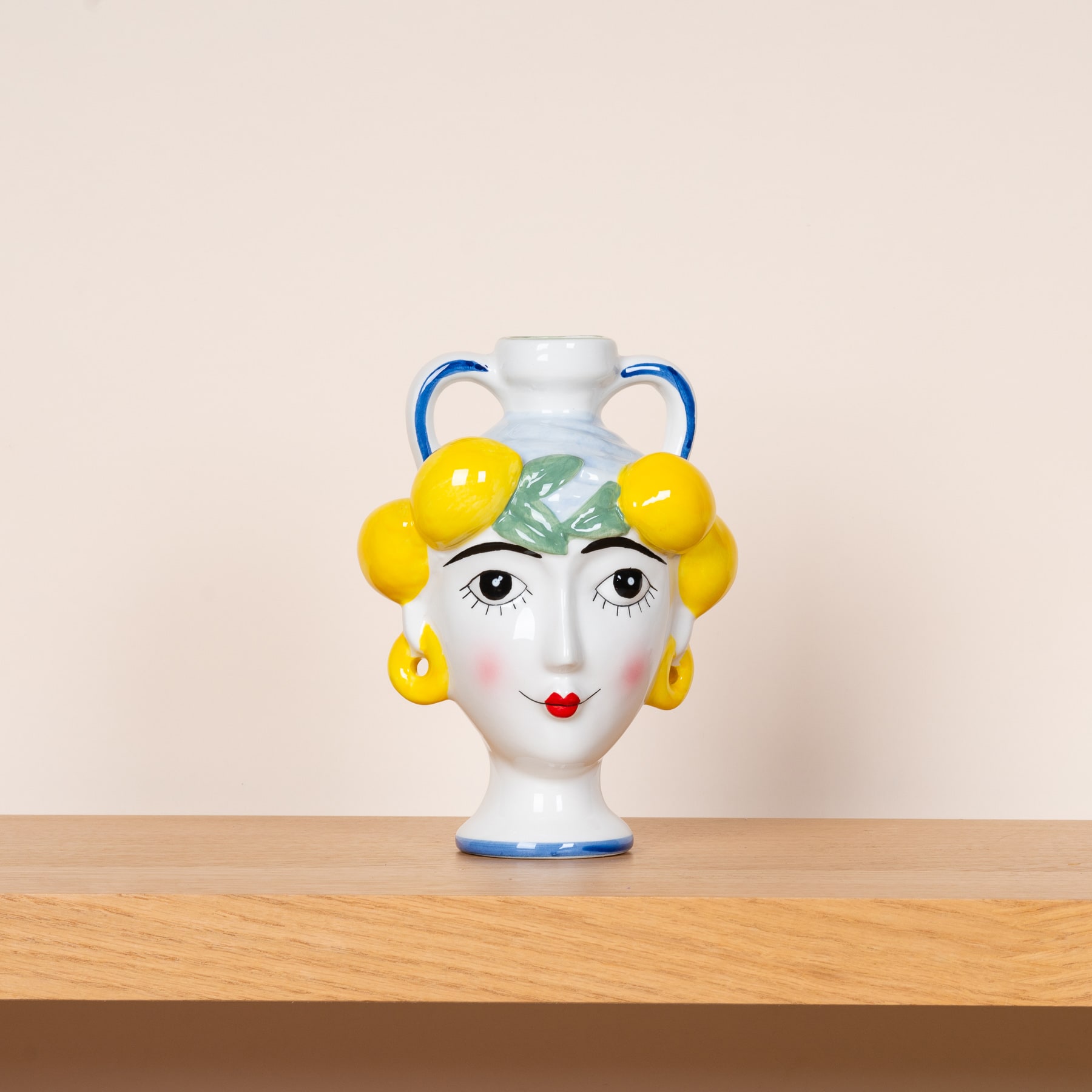 Eine Keramikvase in Form eines Frauenkopfes mit gelben, zitronenähnlichen Objekten, die das Haar schmücken, und einem bemalten Gesicht mit roten Lippen.