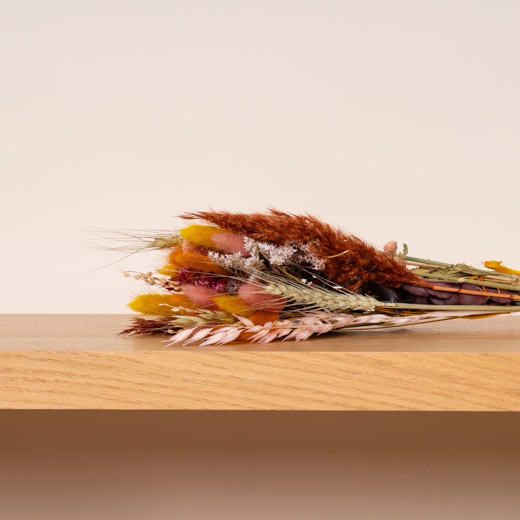 Eine Sammlung getrockneter Weizenhalme, Blumen und anderer natürlicher Elemente, angeordnet auf einer Holzoberfläche vor einem schlichten Hintergrund.