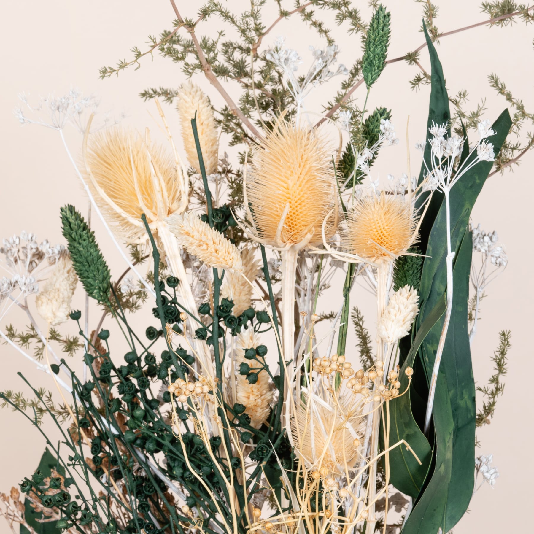 Ein lebendiger Strauß getrockneter Blumen und Grünpflanzen, darunter flauschige gelbe Disteln und zartes Schleierkraut, vor einem neutralen Hintergrund.