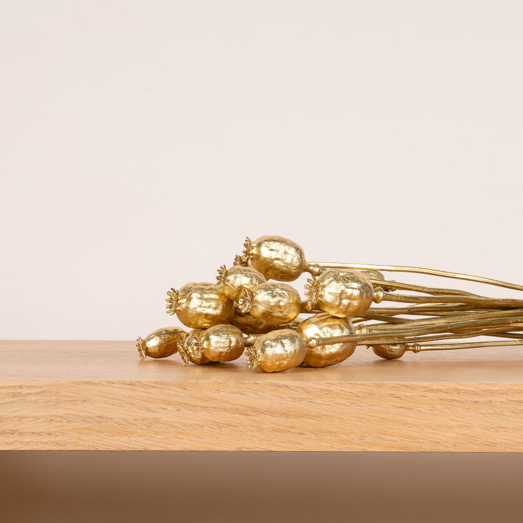 Ein Bündel getrockneter goldfarbener Blumen oder Samenkapseln liegt auf einer Holzoberfläche vor einem schlichten, hellen Hintergrund.