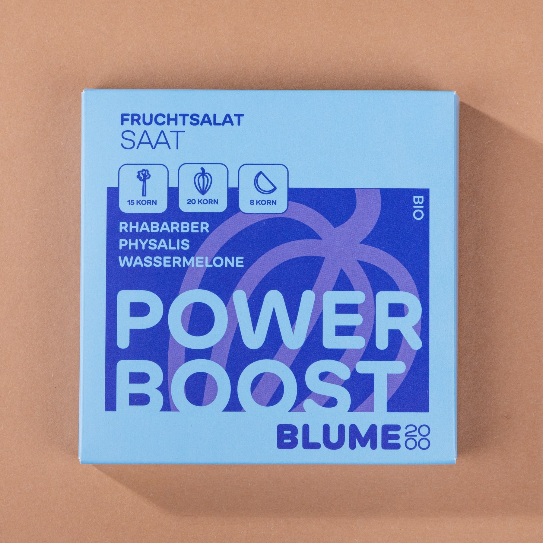 Eine blau-weiße Schachtel mit der Aufschrift „POWER BOOST BLUME 2020“ und Symbolen von Rhabarber, Physalis und Wassermelone auf pfirsichfarbenem Hintergrund.