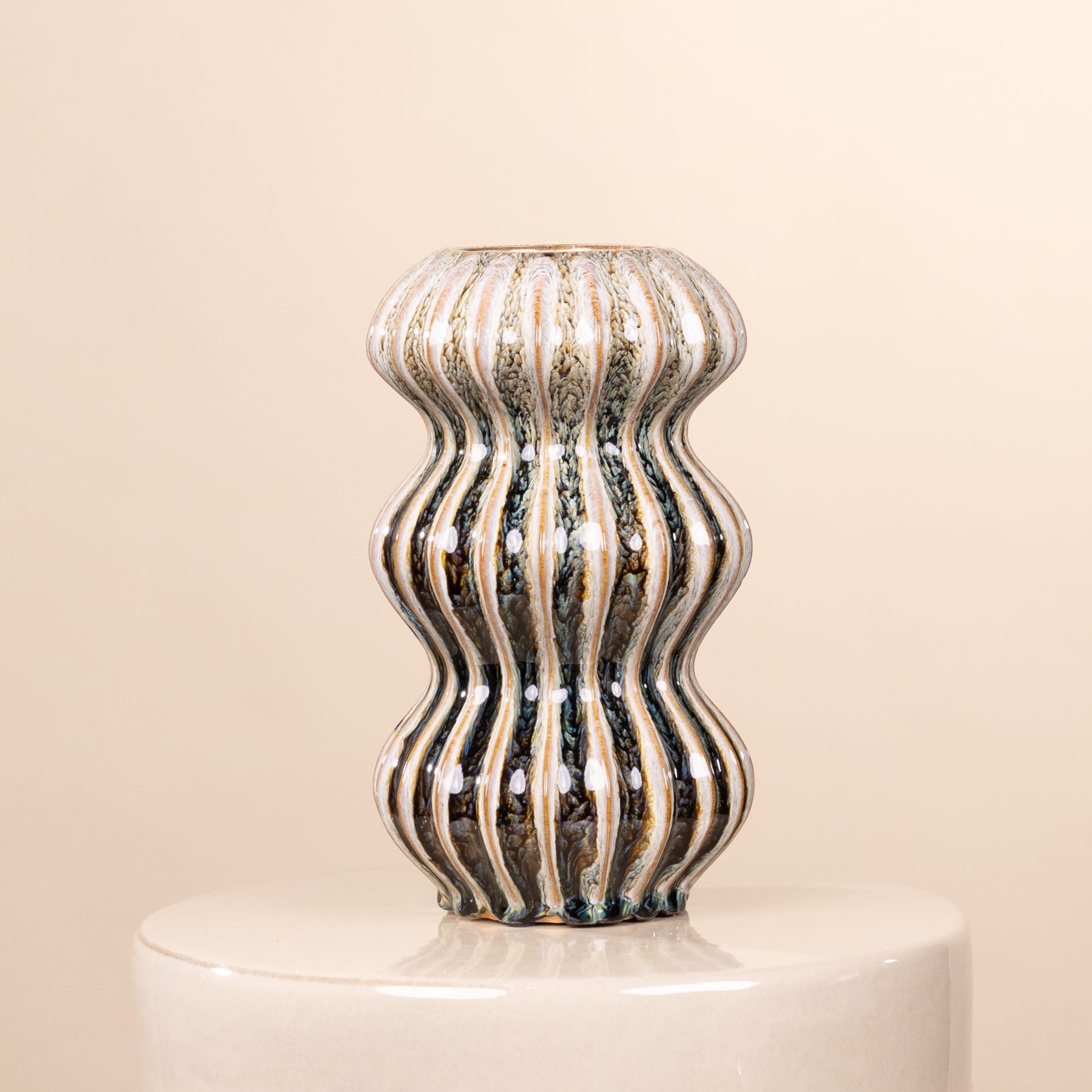 Eine Glasvase mit einem einzigartigen, wellenförmigen Muster steht auf einem weißen Sockel vor einem beigen Hintergrund.