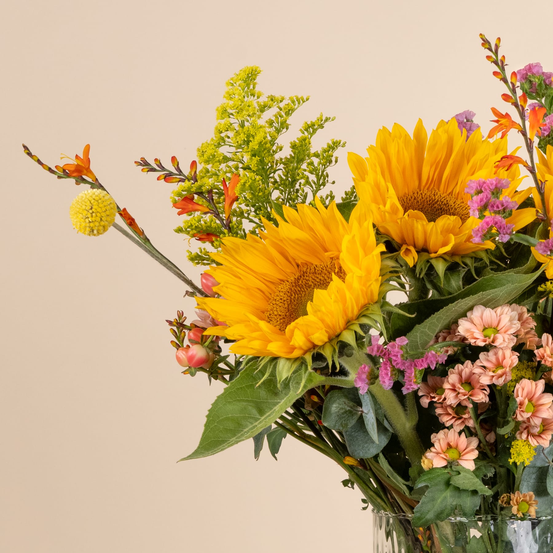 Ein lebendiger Strauß aus Sonnenblumen, Gänseblümchen und anderen bunten Blumen vor einem neutralen beigen Hintergrund.