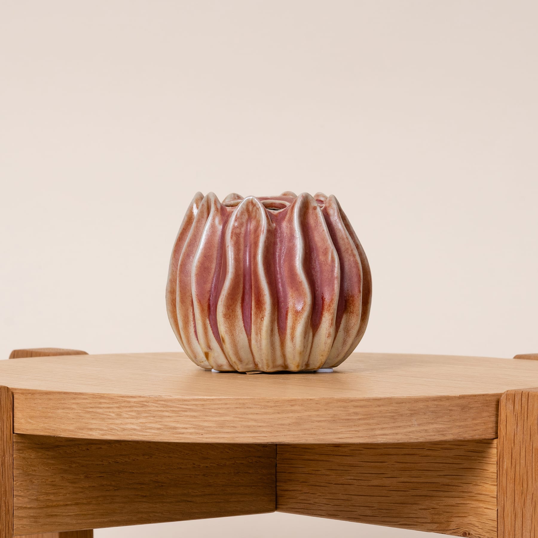 Eine Keramikvase mit einem einzigartigen, abstrakten Blumenmuster steht auf einer Holzoberfläche vor einem schlichten, beigen Hintergrund.