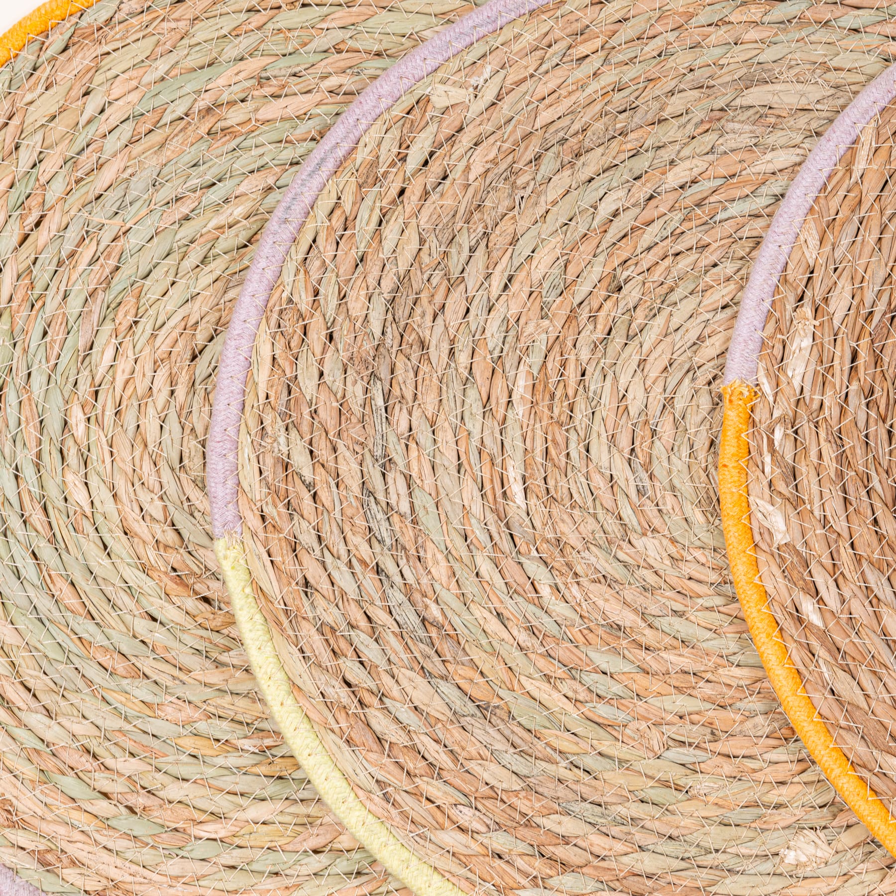 Das Bild zeigt eine Nahaufnahme von gewebten Stroh- oder Rattanmatten und zeigt ihre komplizierten und sich überlappenden Muster in Beige-, Orange- und Gelbtönen.