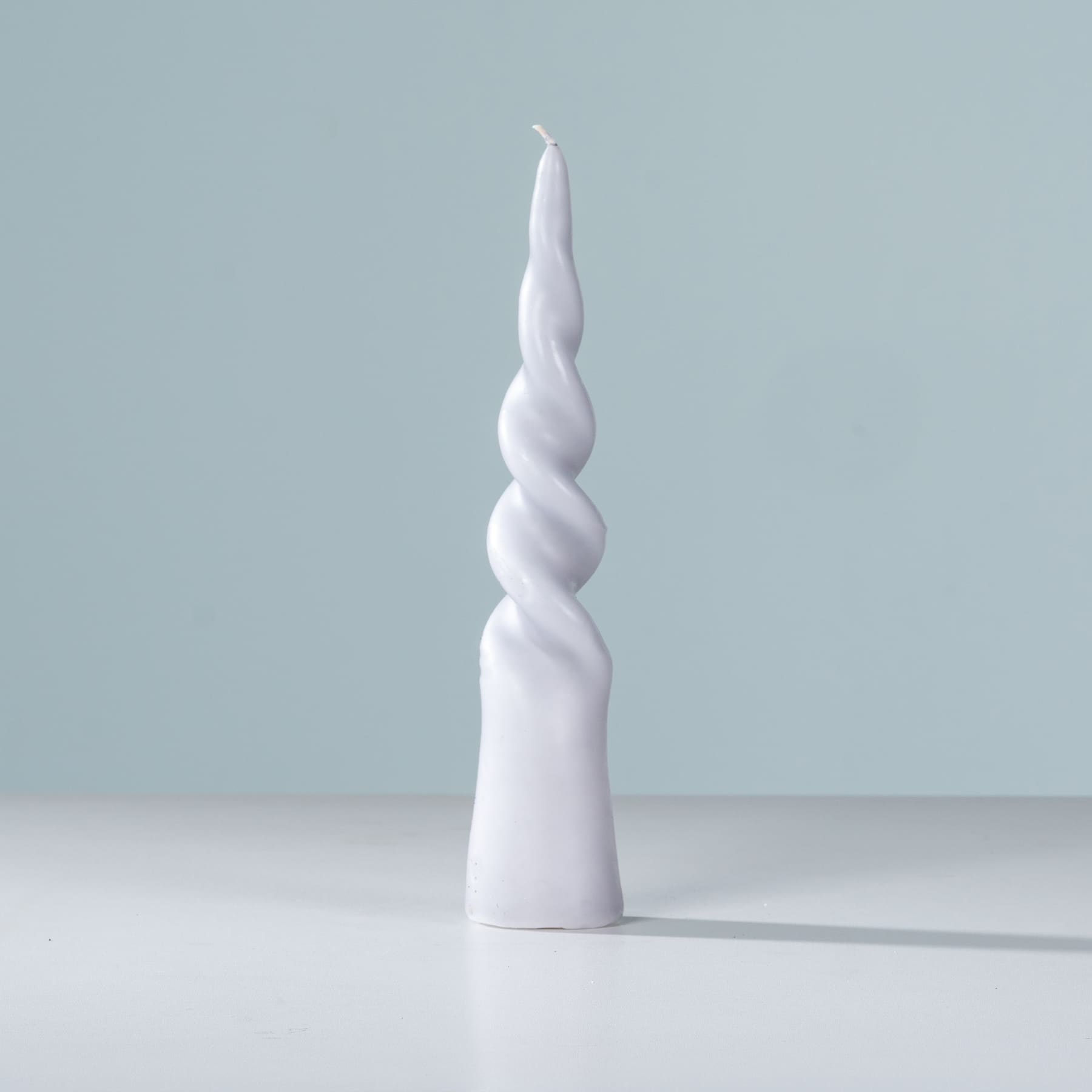 Eine große, gedrehte weiße Keramikskulptur steht auf einer schlichten weißen Oberfläche vor einem hellblauen Hintergrund.