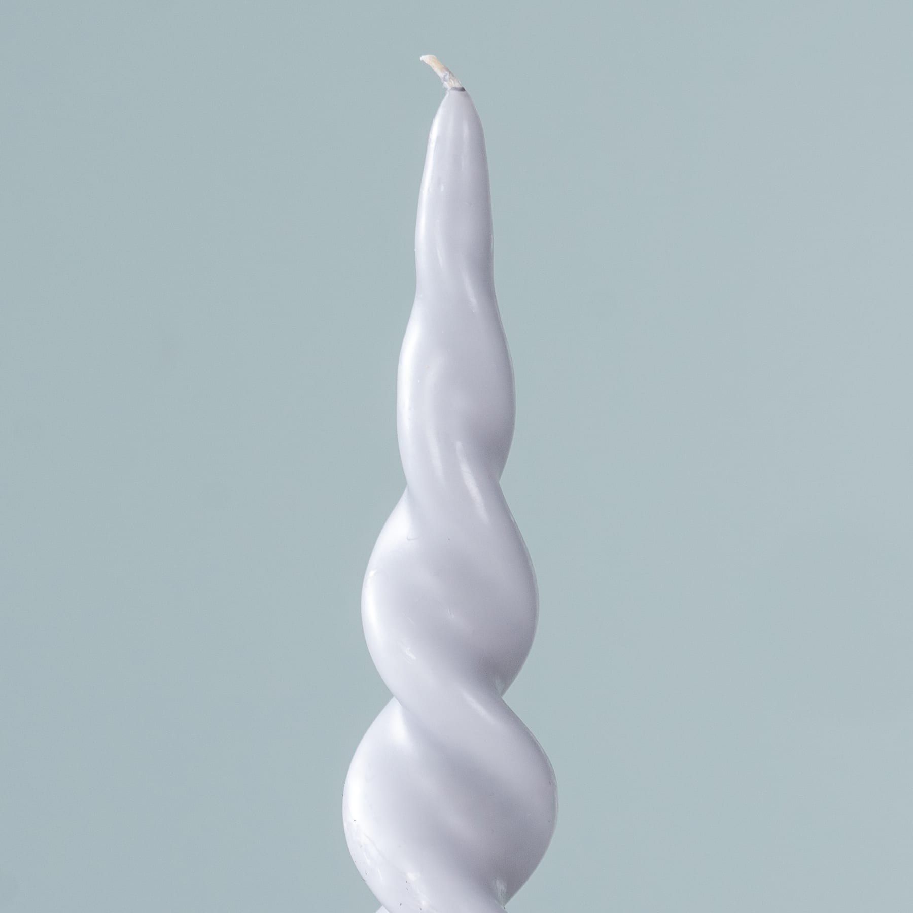 Eine weiße, spiralförmige Kerze steht vor einem hellblauen Hintergrund.