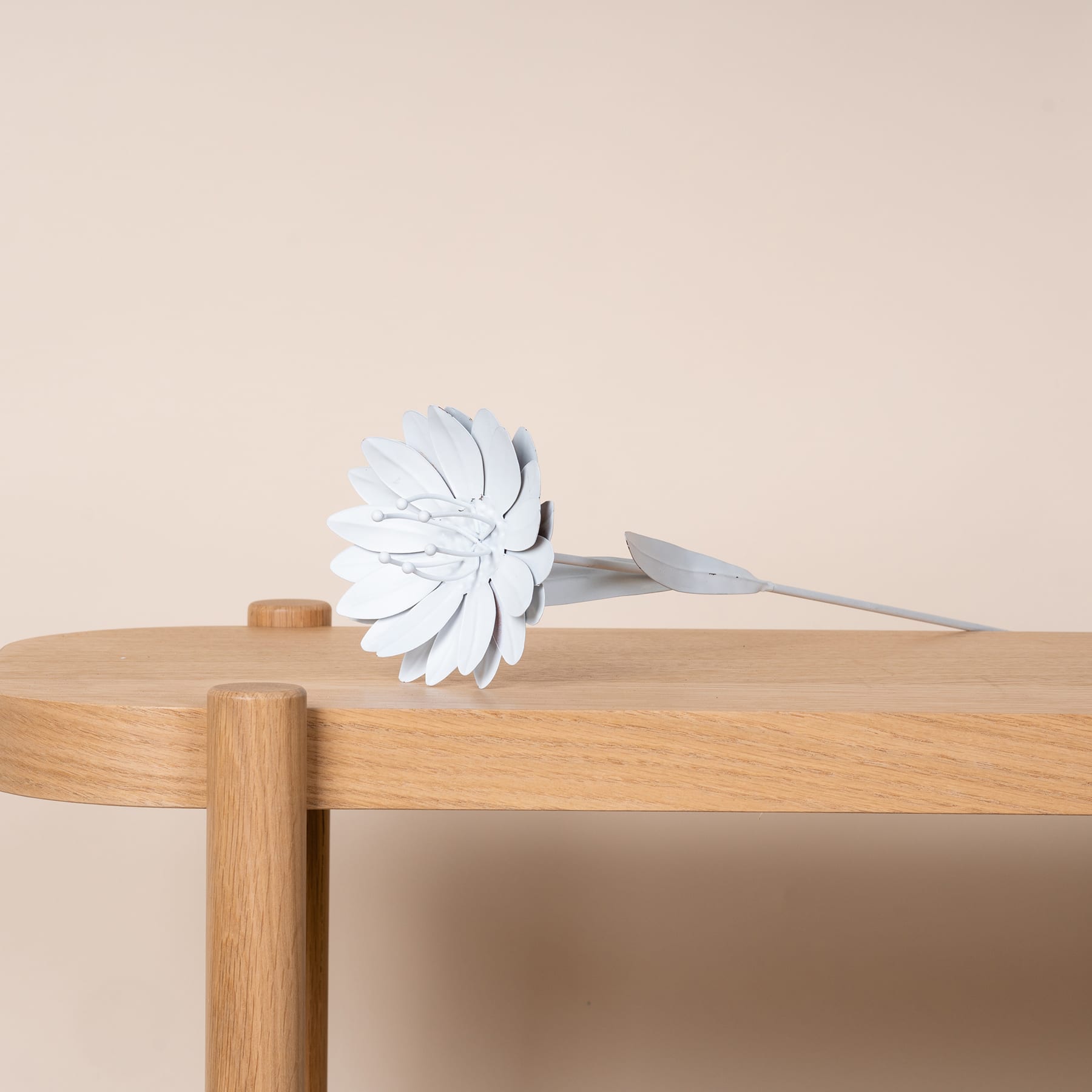 Eine weiße Papierblume liegt auf einem Holztisch vor einem beigen Hintergrund.