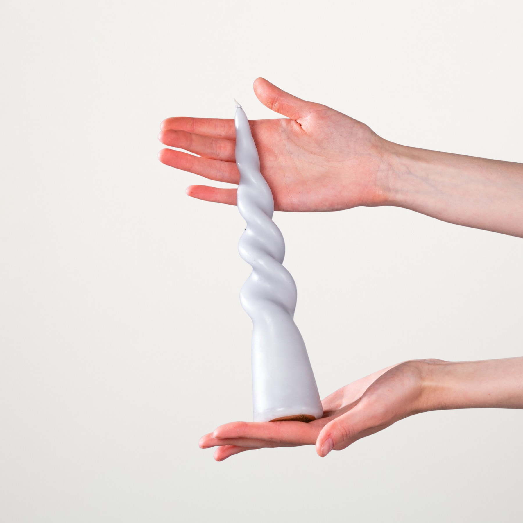 Hände halten ein gedrehtes weißes Tuch vor einem schlichten weißen Hintergrund.