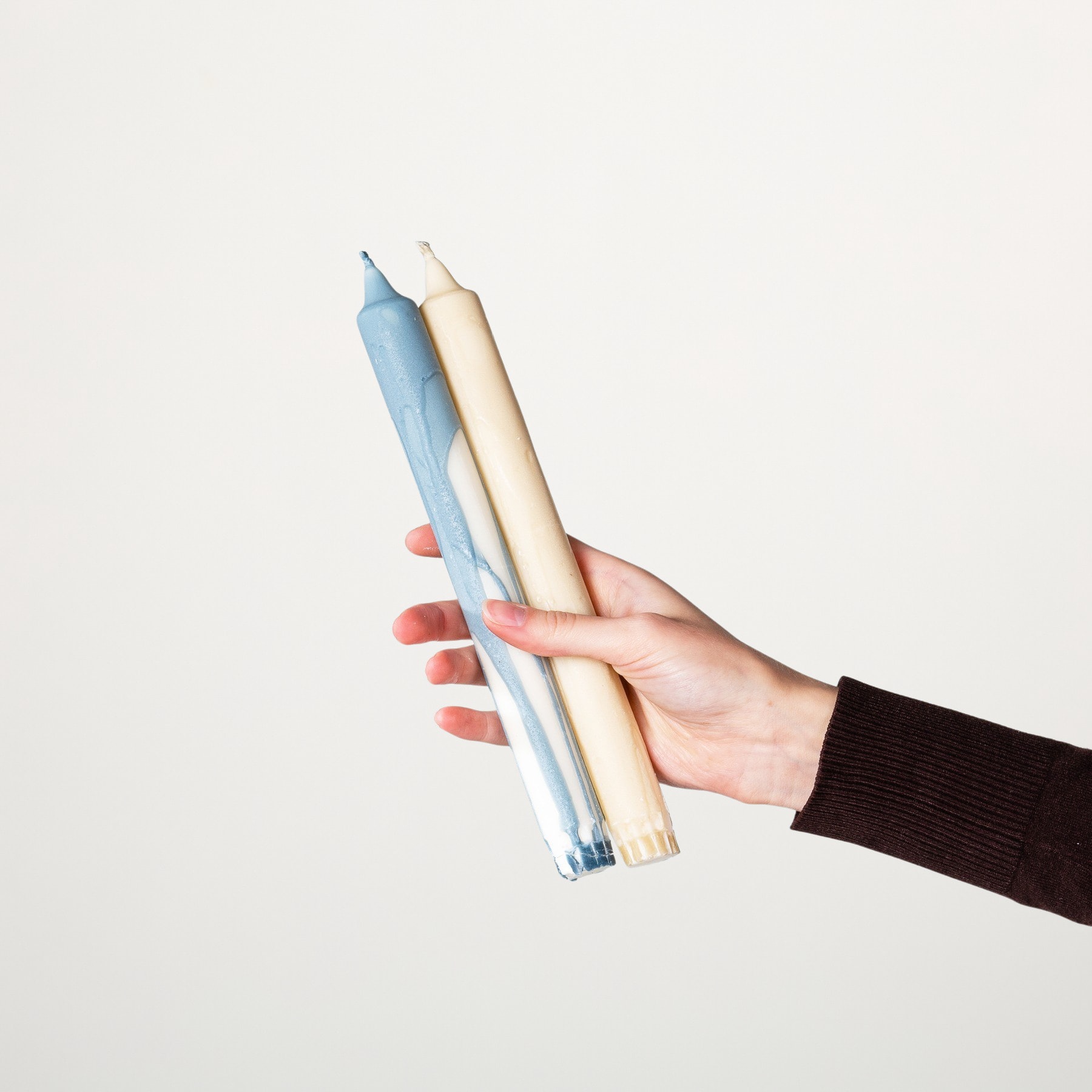 Eine Hand hält zwei Buntstifte, einen blauen und einen beigen, vor einem schlichten weißen Hintergrund.