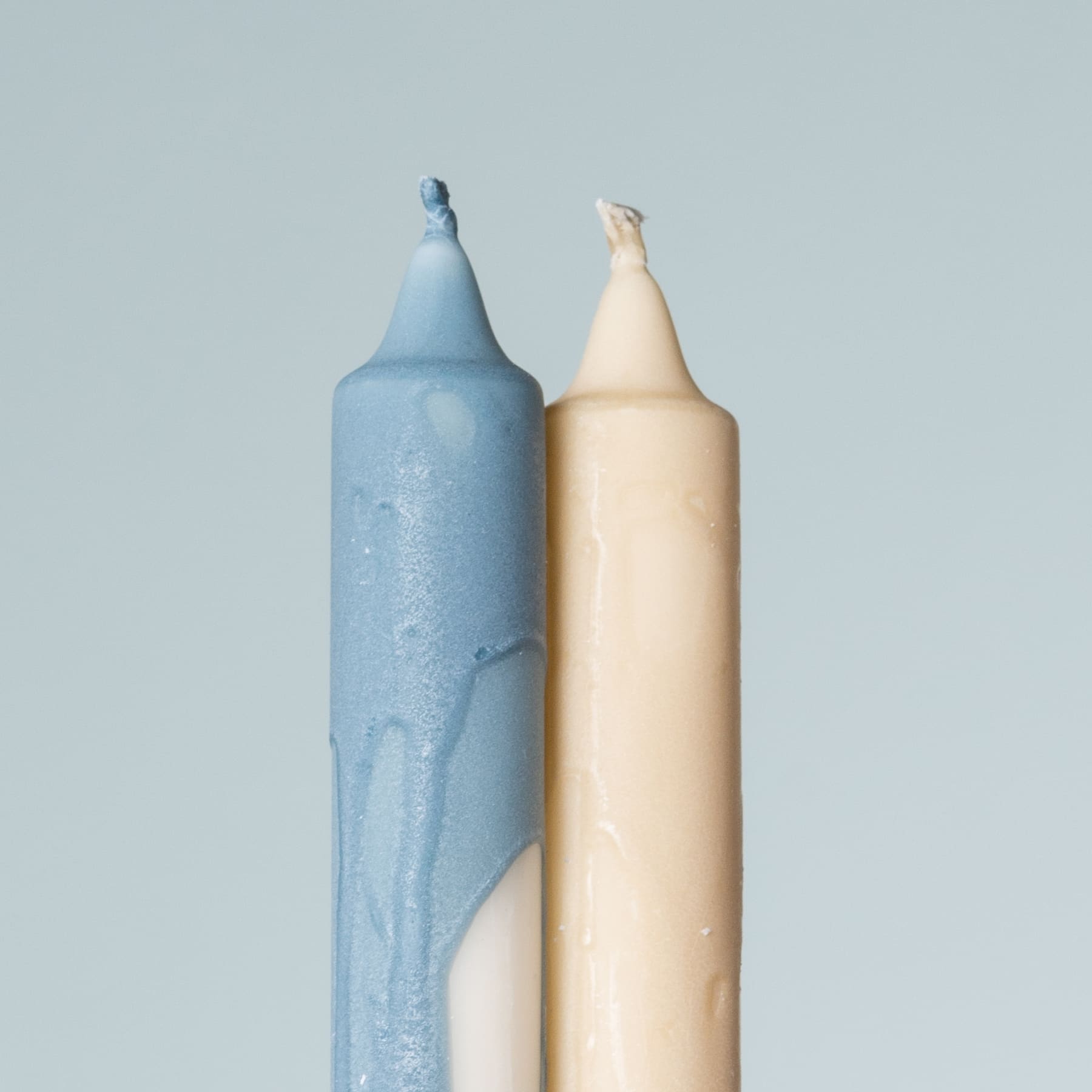 Zwei Buntstifte, einer blau und einer beige, stehen aufrecht vor einem hellblauen Hintergrund.