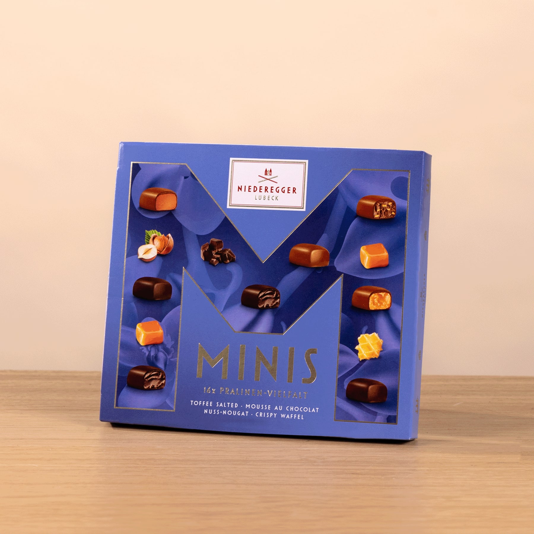 Auf einer Holzoberfläche steht eine blaue Schachtel mit verschiedenen Miniatur-Schokoladenbonbons.
