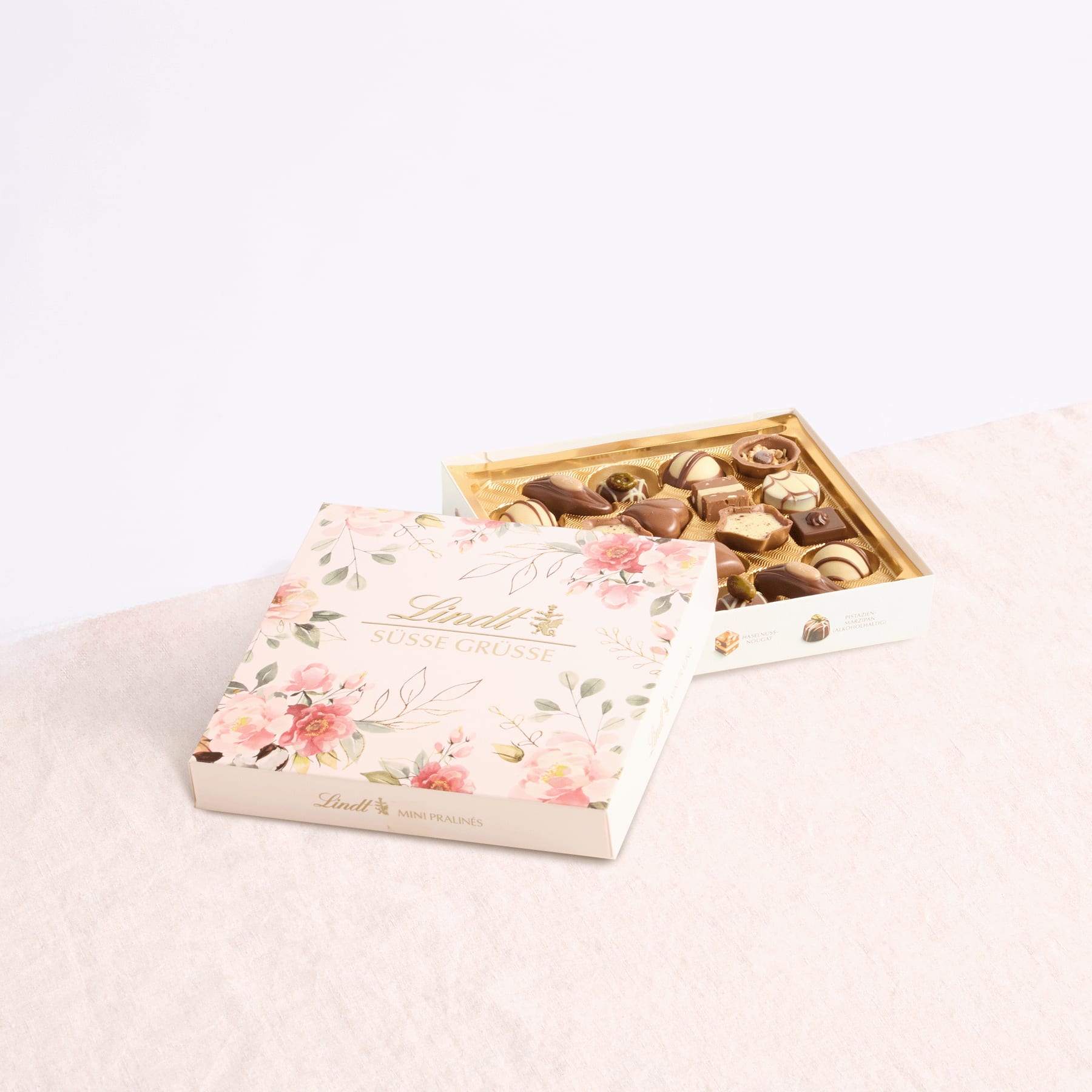 Auf einer hellen Oberfläche steht eine dekorative Schachtel mit verschiedenen Pralinen, und der Deckel mit Blumenmuster verleiht der Szene einen Hauch von Eleganz.