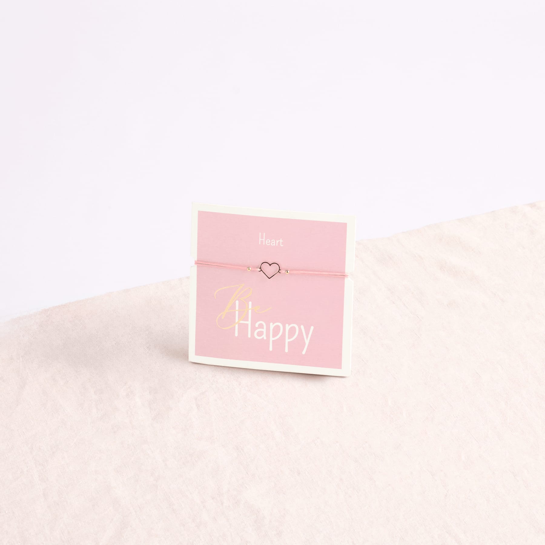 Ein rosa Umschlag mit der Aufschrift „Happy“ liegt auf einer weichen, flauschigen weißen Oberfläche.