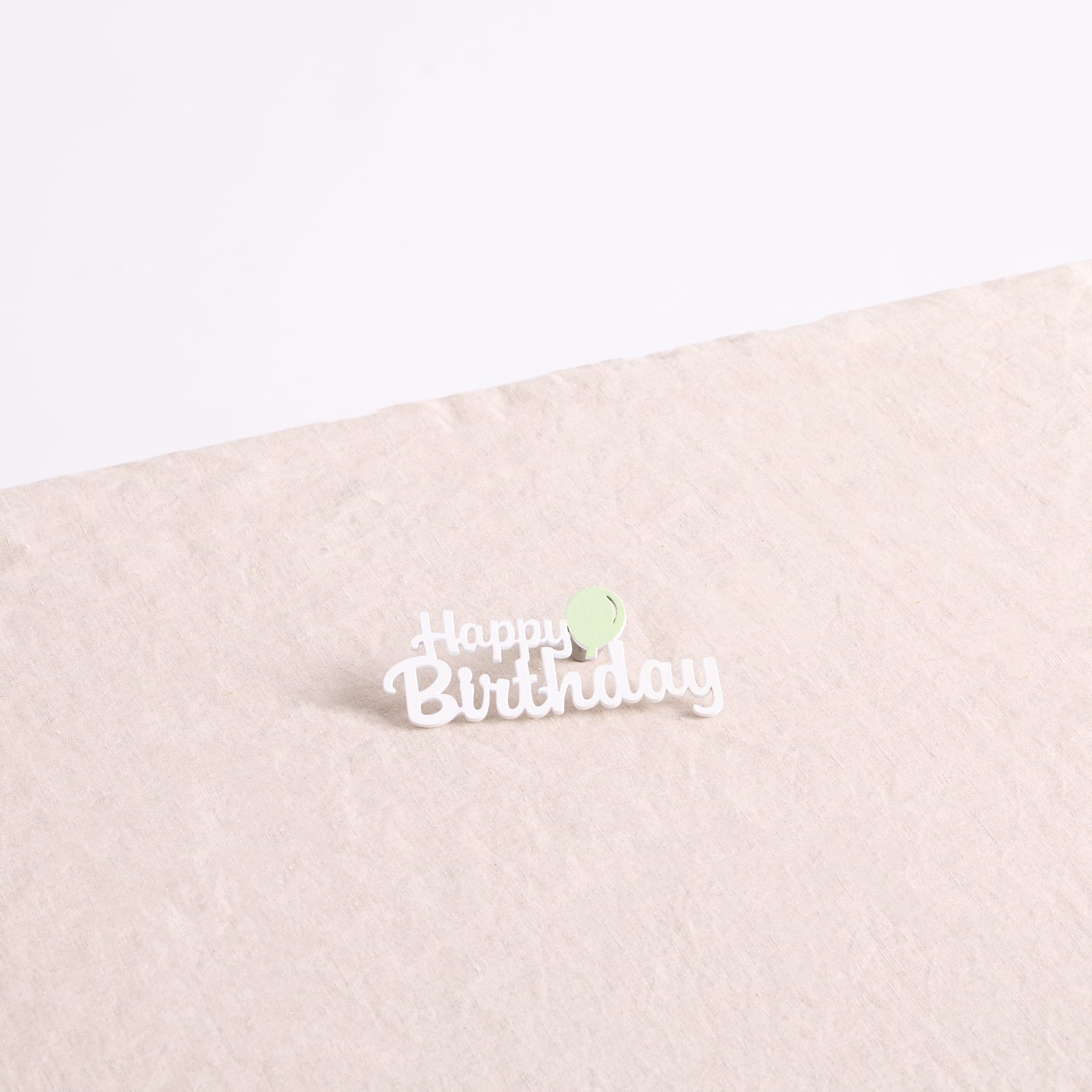 Auf einem beigen Hintergrund befindet sich ein weißer „Happy Birthday“-Text mit einer grünen kerzenähnlichen Form.